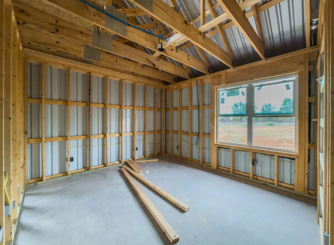 Exposed wooden framing, concrete flooring, corrugated metal walls, and a large window