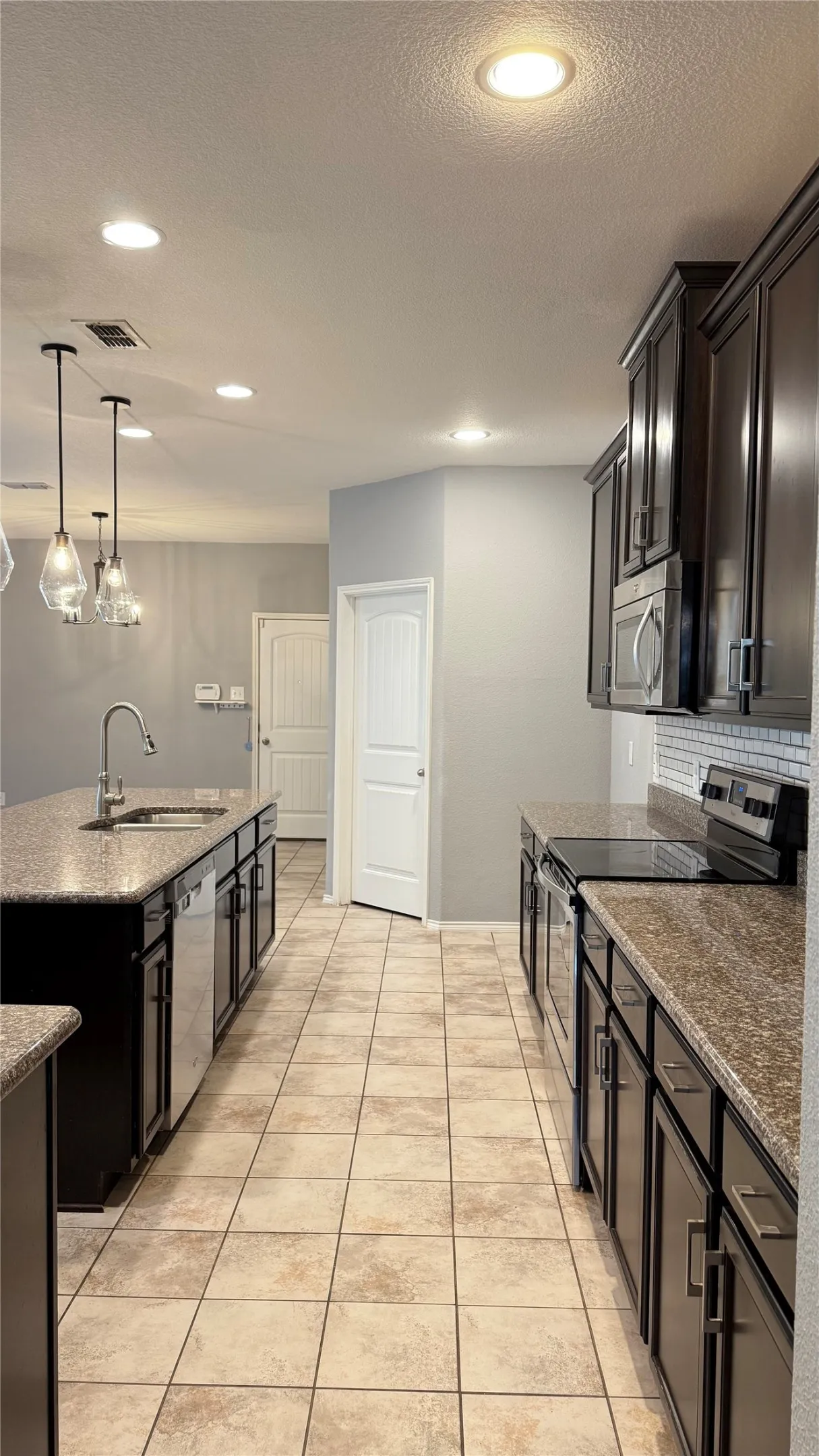 Kitchen featuring stainless steel appliances, a sink, a center island with sink, backsplash, and a textured ceiling