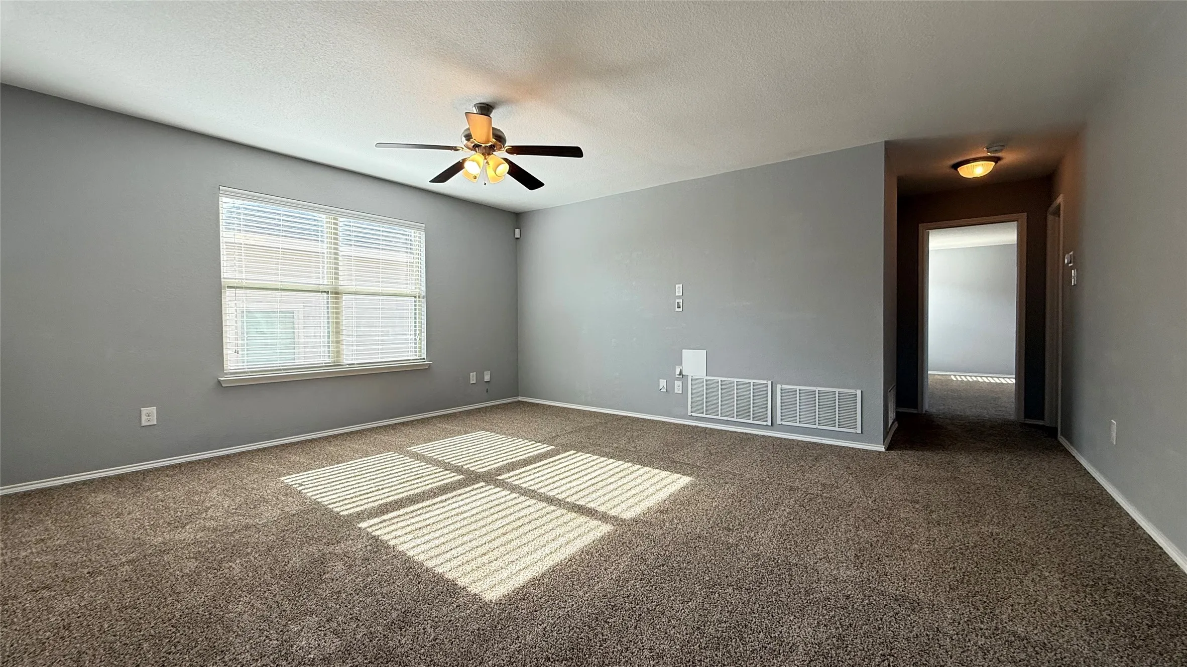 Carpeted spare room with a ceiling fan, baseboards, and a textured ceiling