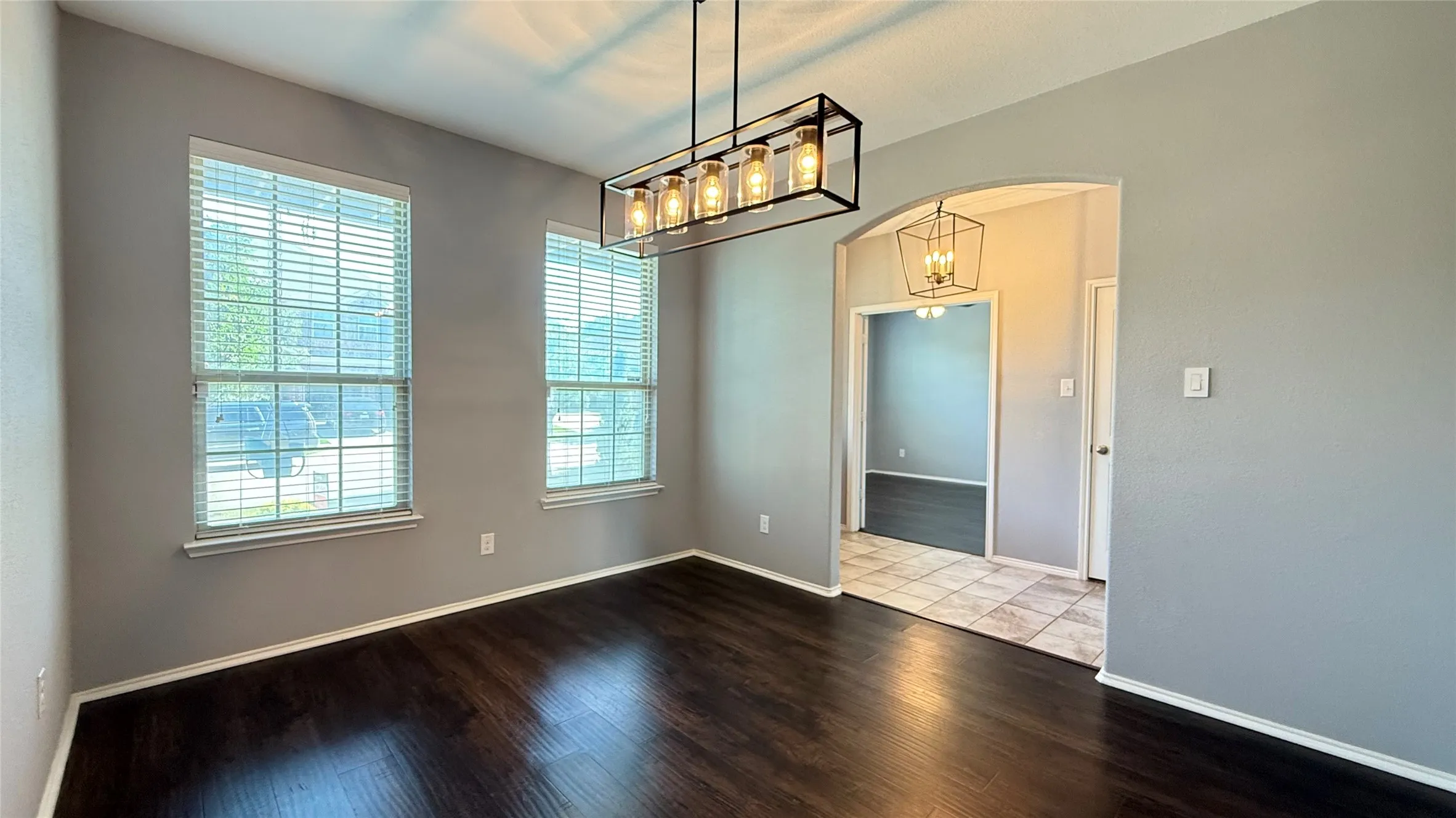 Spare room featuring arched walkways, wood finished floors, a chandelier, and baseboards