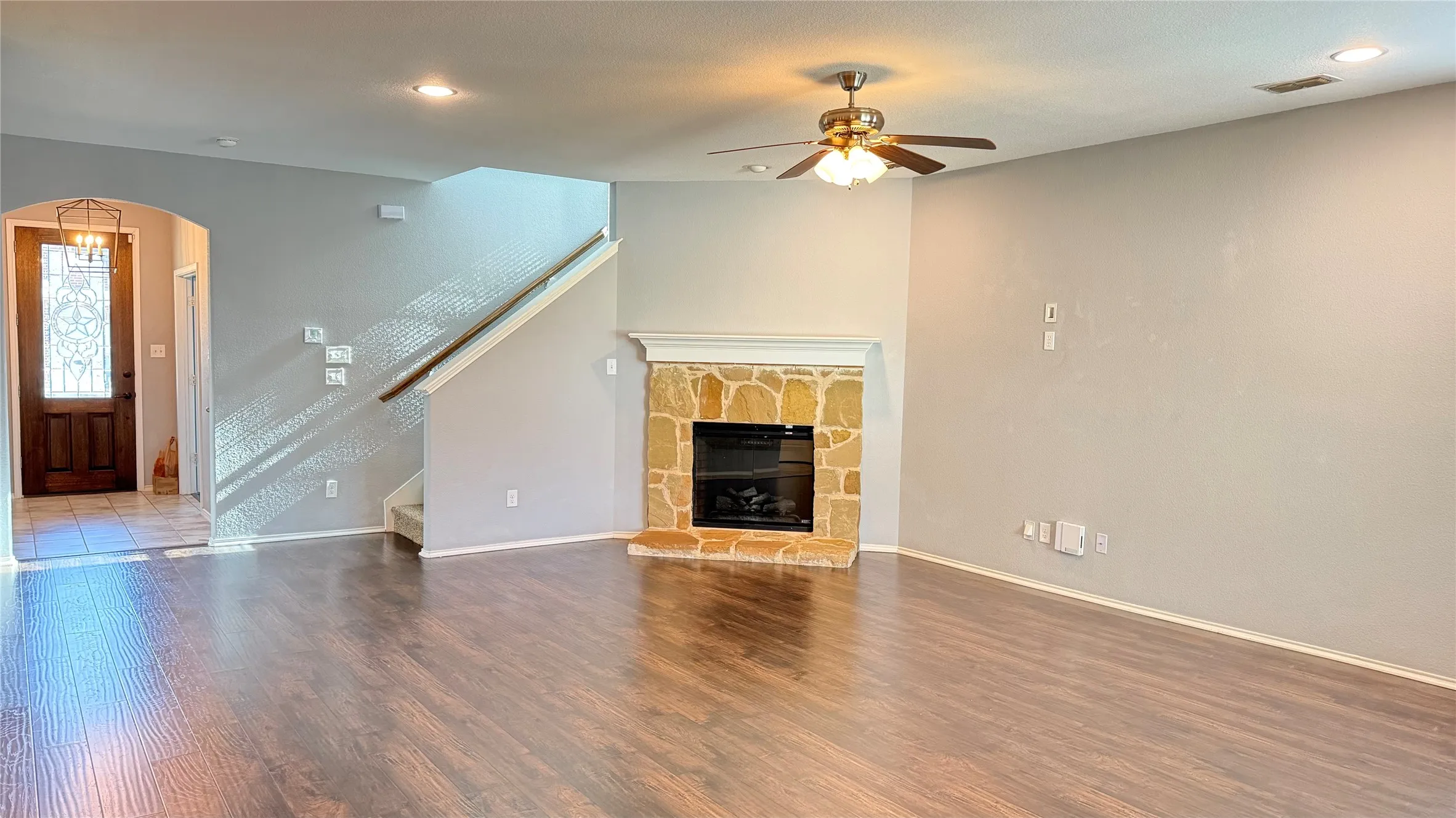 Unfurnished living room with ceiling fan, wood finished floors, arched walkways, stairs, and baseboards