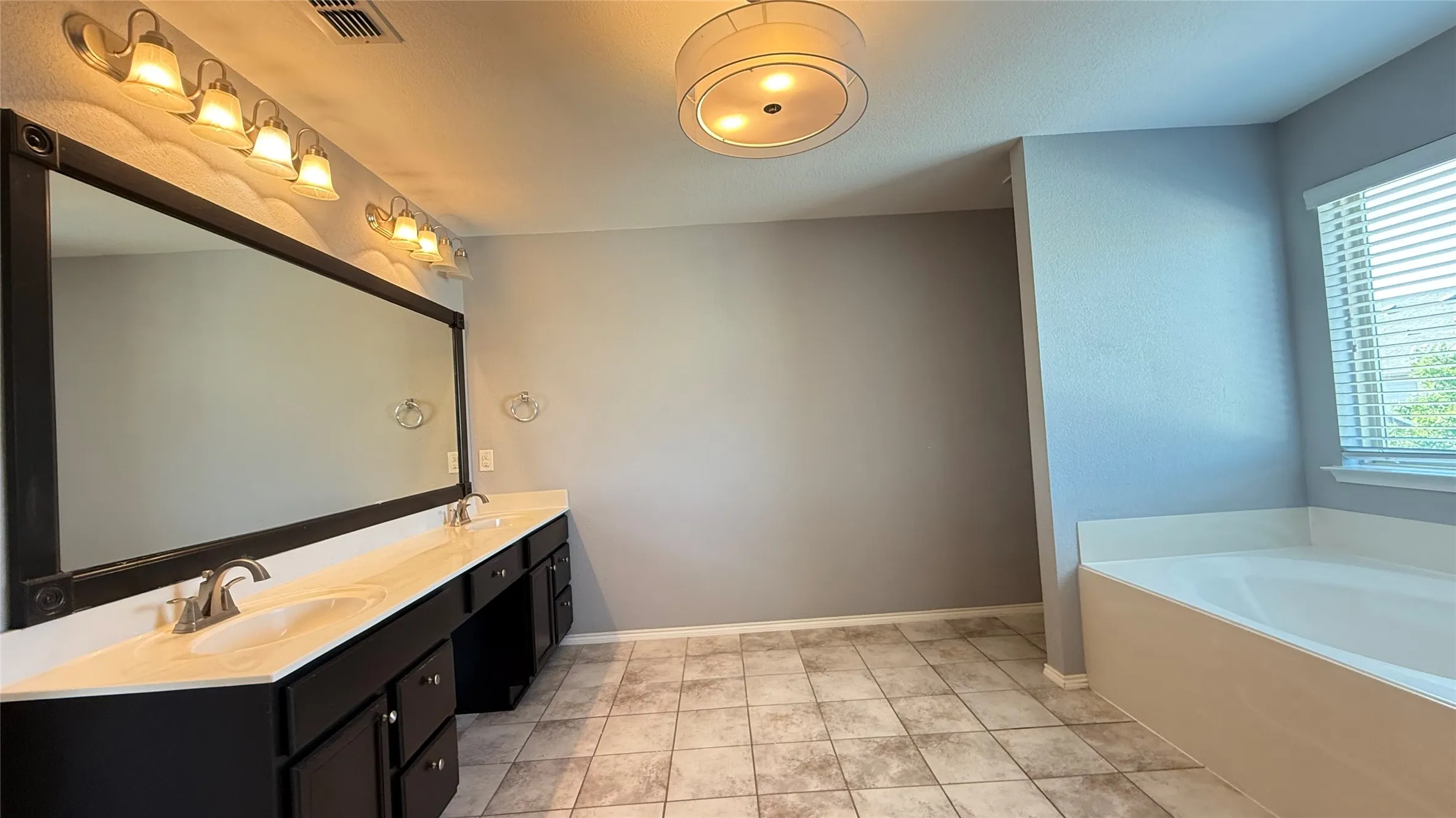 Full bath featuring double vanity, a garden tub, and baseboards
