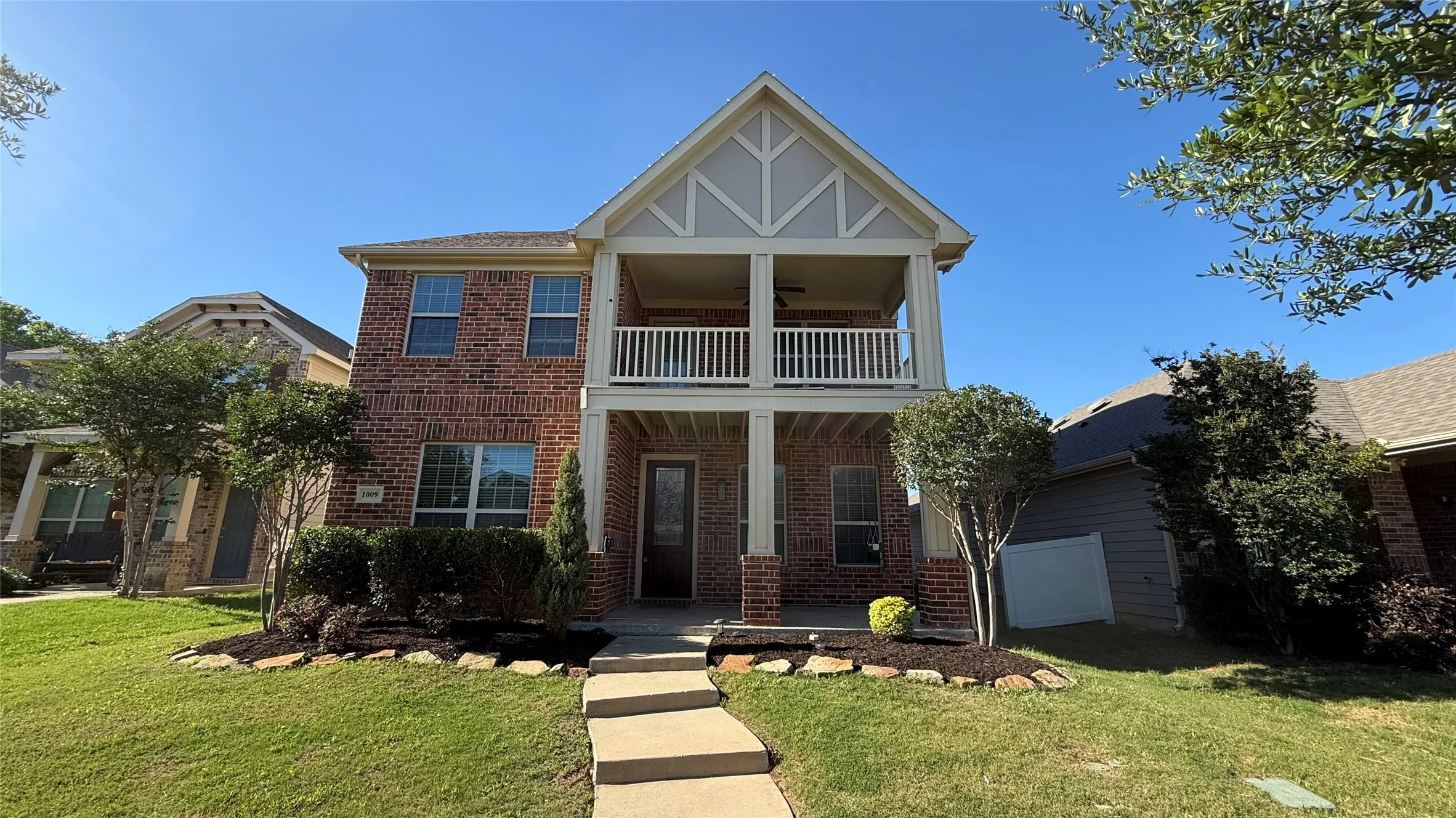 View of front facade with a balcony, brick siding, and a front lawn
