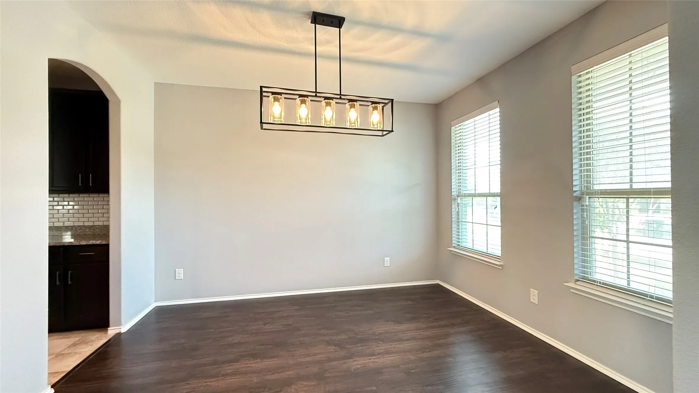 Unfurnished dining area featuring plenty of natural light, dark wood finished floors, arched walkways, and baseboards