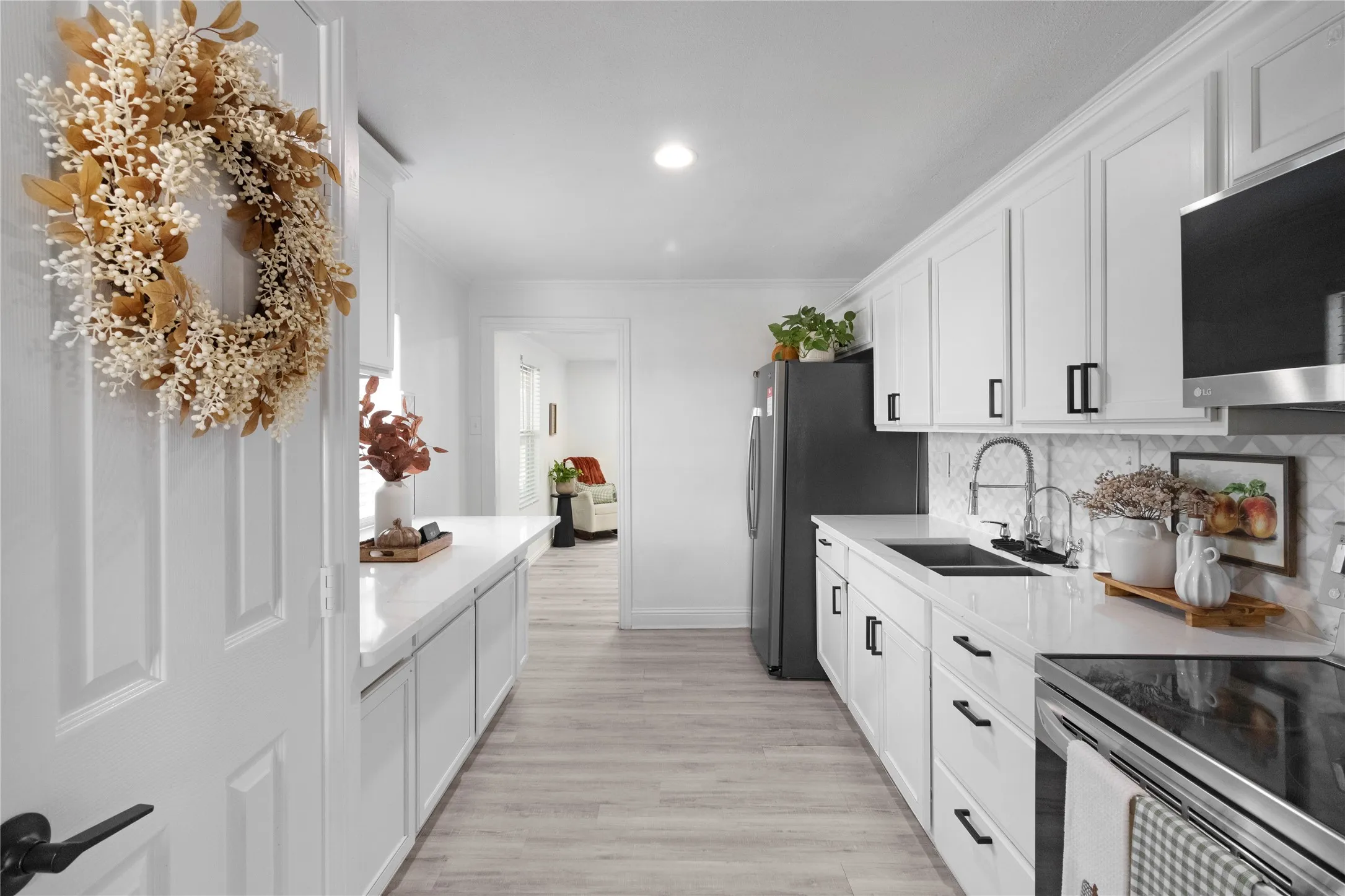 White shaker-style cabinetry, light-toned wood-finish flooring, recessed lighting, and a patterned tile backsplash