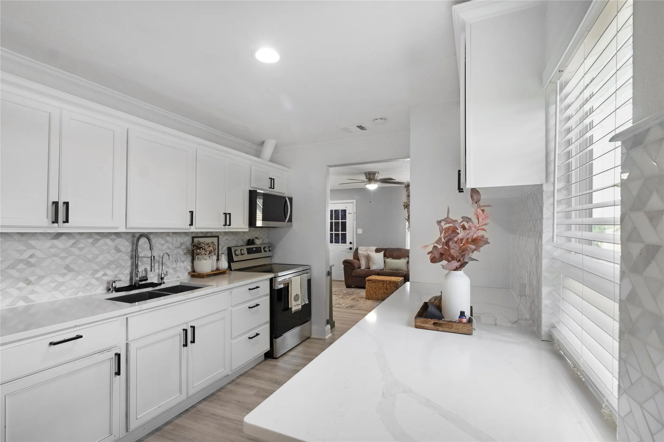 White shaker-style cabinetry with matte black hardware, quartz countertops, patterned tile backsplash, stainless steel appliances, and wood-finish flooring