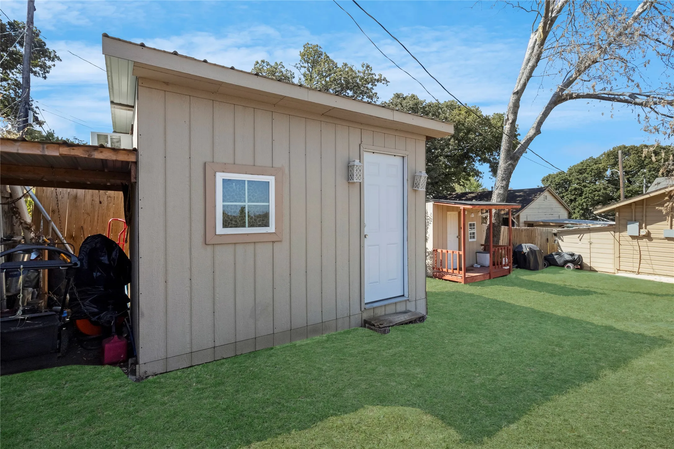 Expansive backyard featuring a manicured lawn, a detached storage shed with a window and exterior lighting, and an additional smaller structure with a covered porch and railings