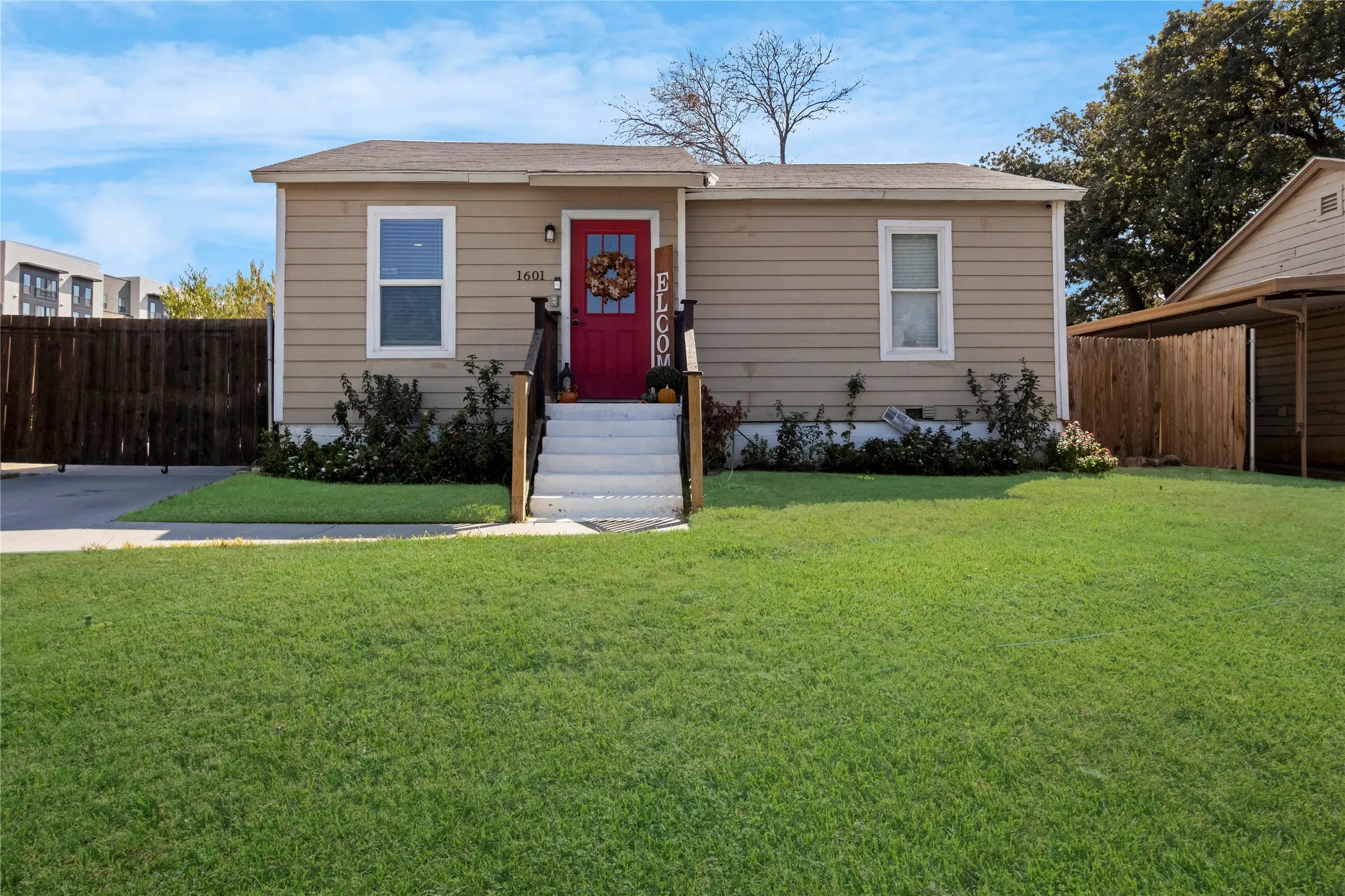 Exterior featuring beige siding, a red front door, white trim windows, and a paved driveway