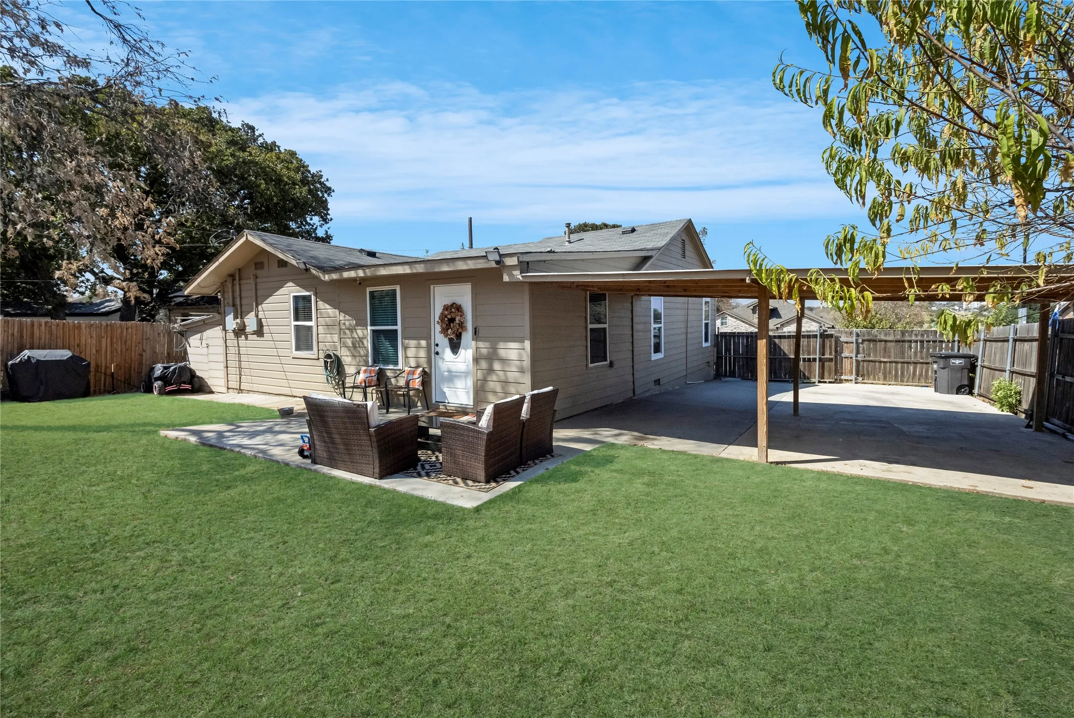 Expansive grassy lawn, concrete patio, covered concrete parking area, wooden privacy fence, and siding exterior