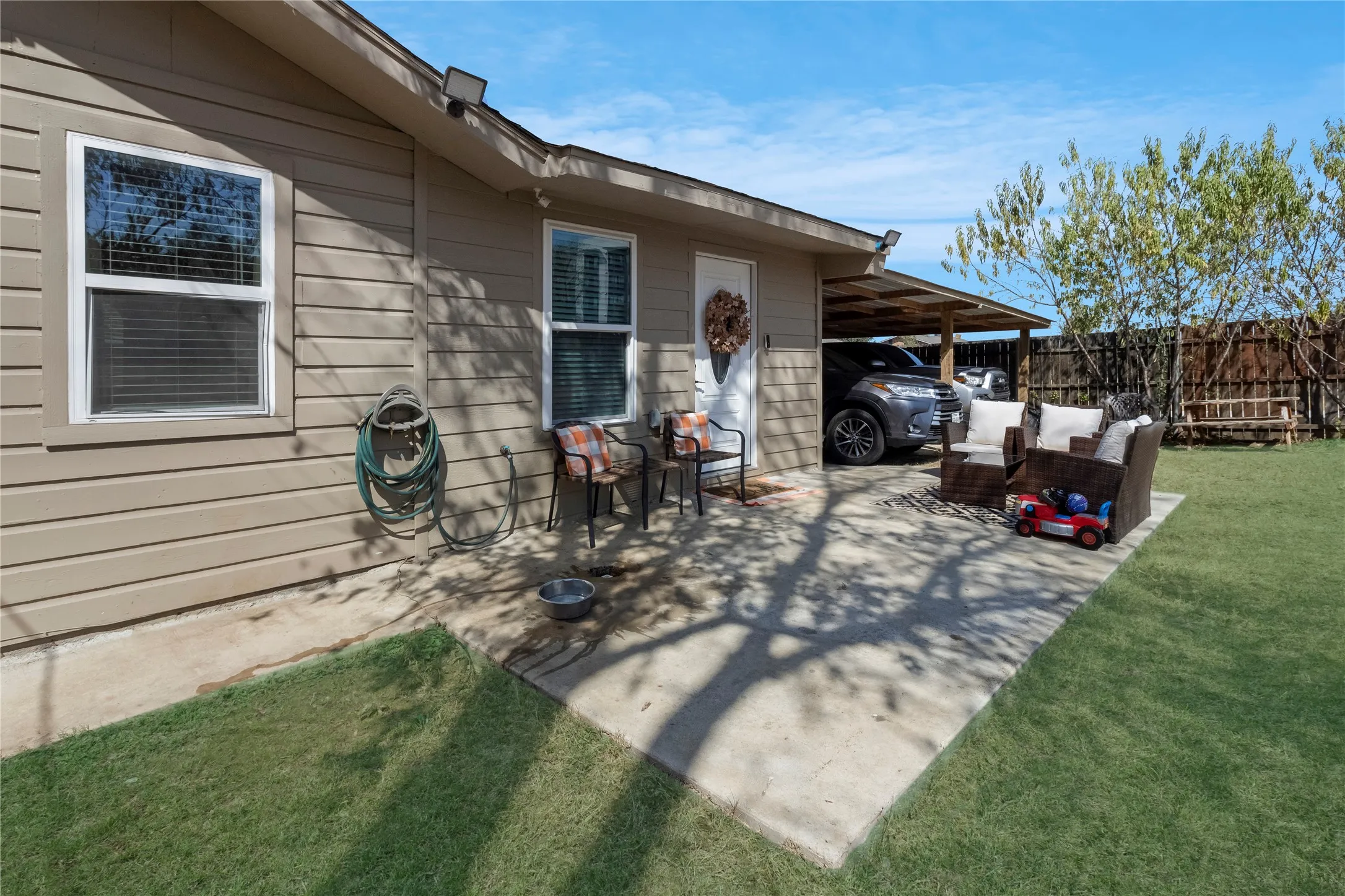 Carport structure, concrete patio, tan horizontal siding, privacy fencing, and a manicured lawn