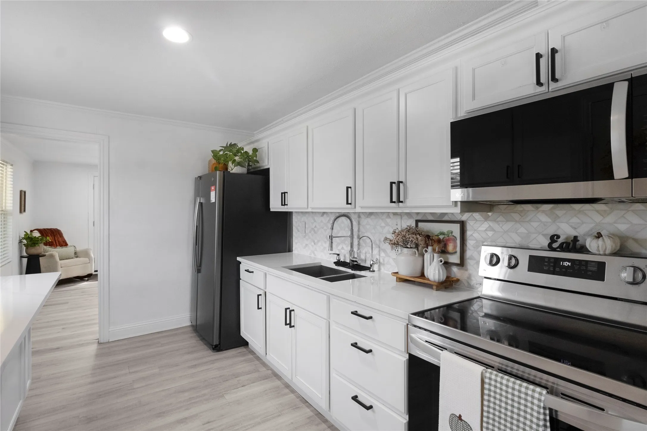 White shaker-style cabinetry with matte black hardware, stainless steel appliances, and a mosaic tile backsplash