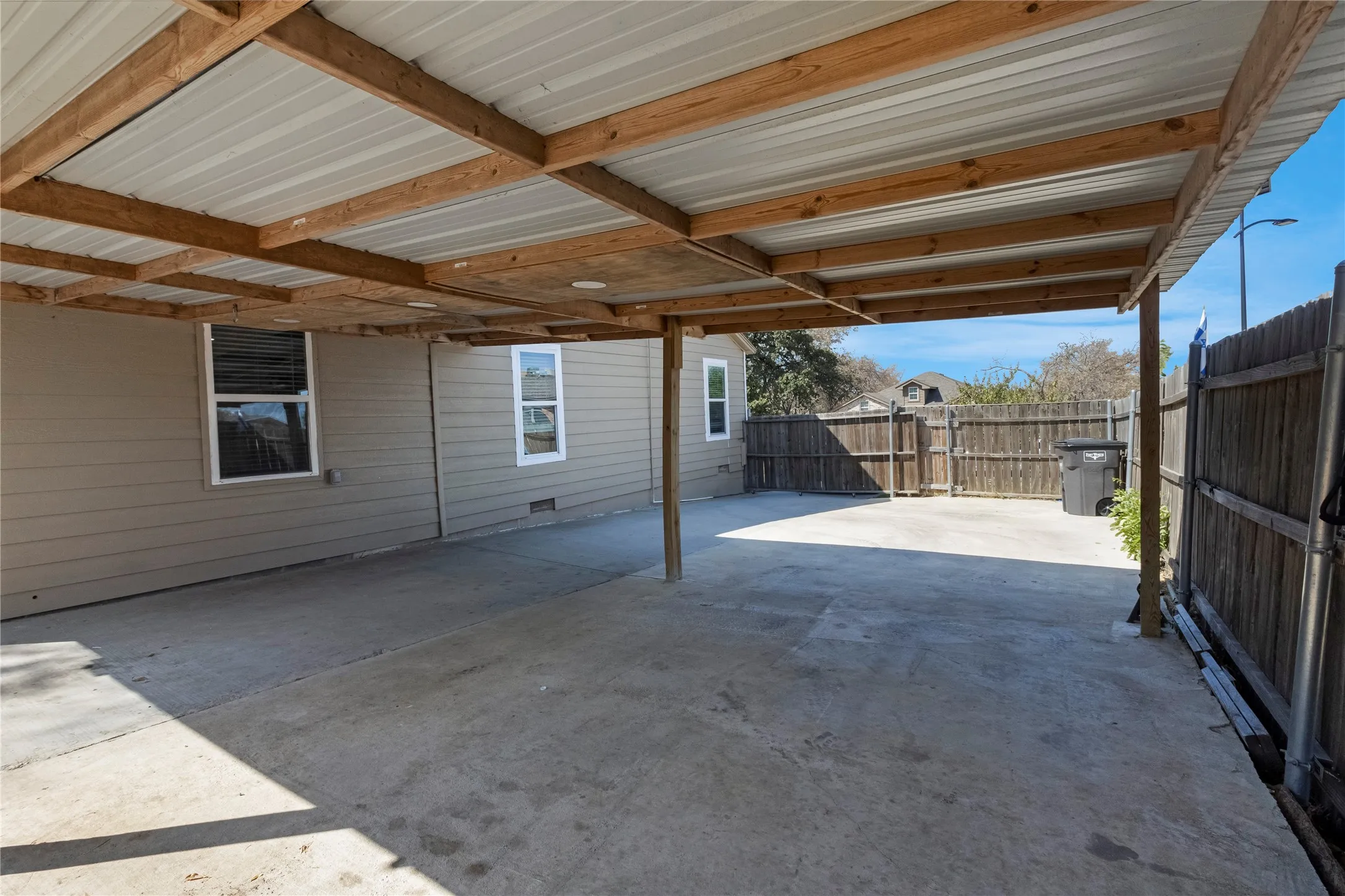 Carport featuring a metal roof, wood beam construction, and concrete flooring