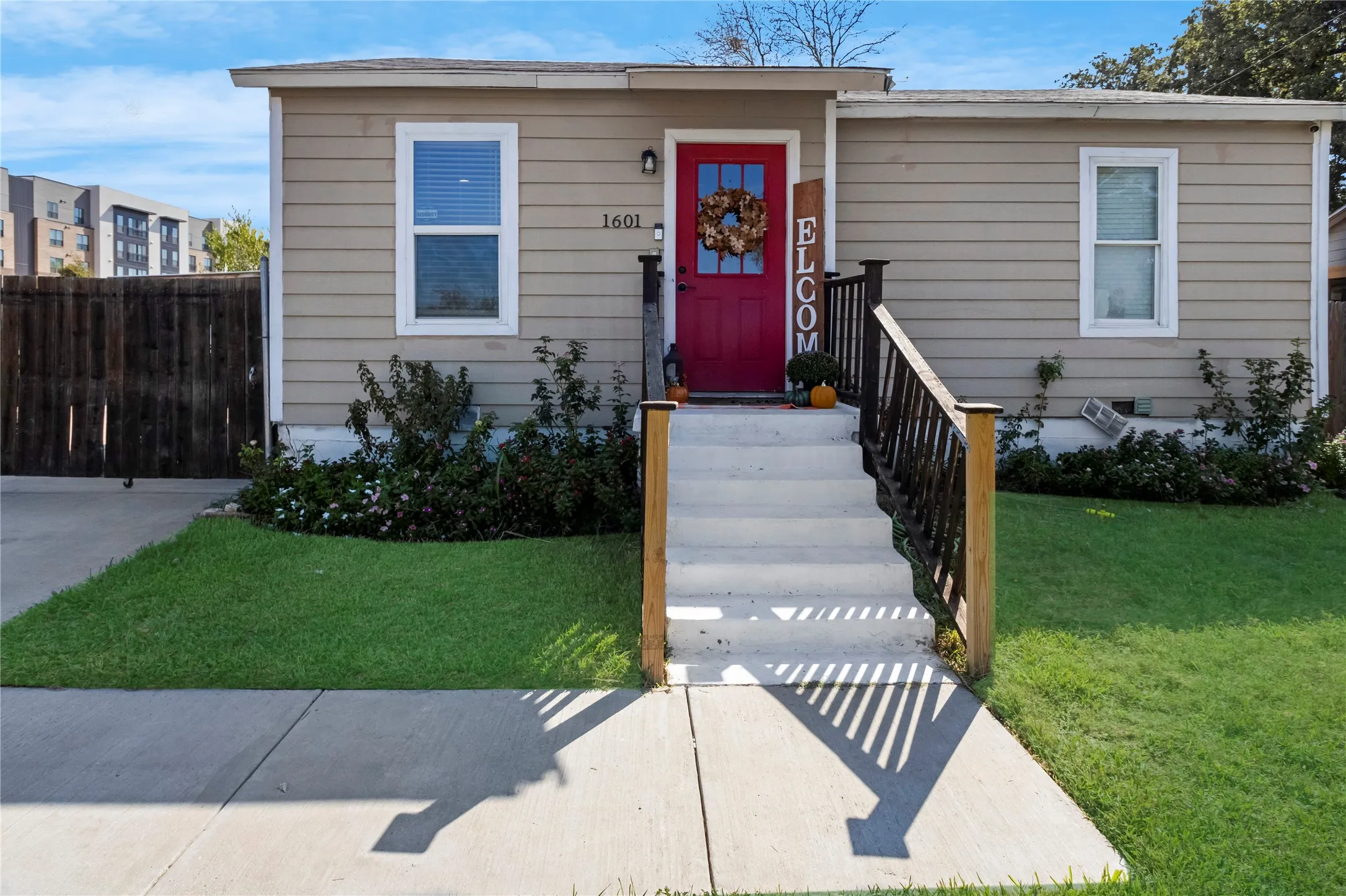 Siding exterior with a vibrant red entry door, white trim windows, and a concrete pathway leading to the entrance