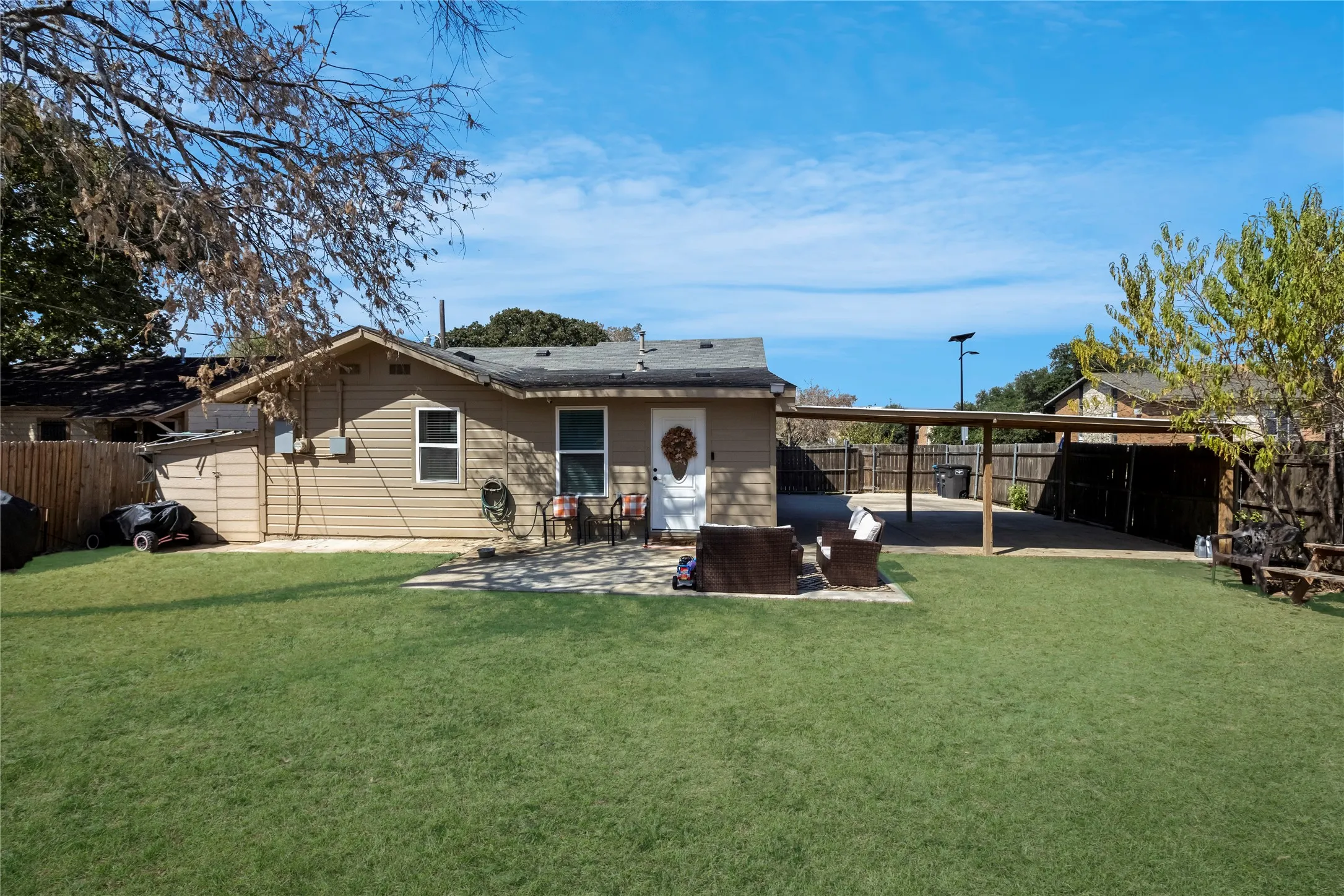 Expansive grassy yard with a concrete patio, attached carport, and privacy fencing