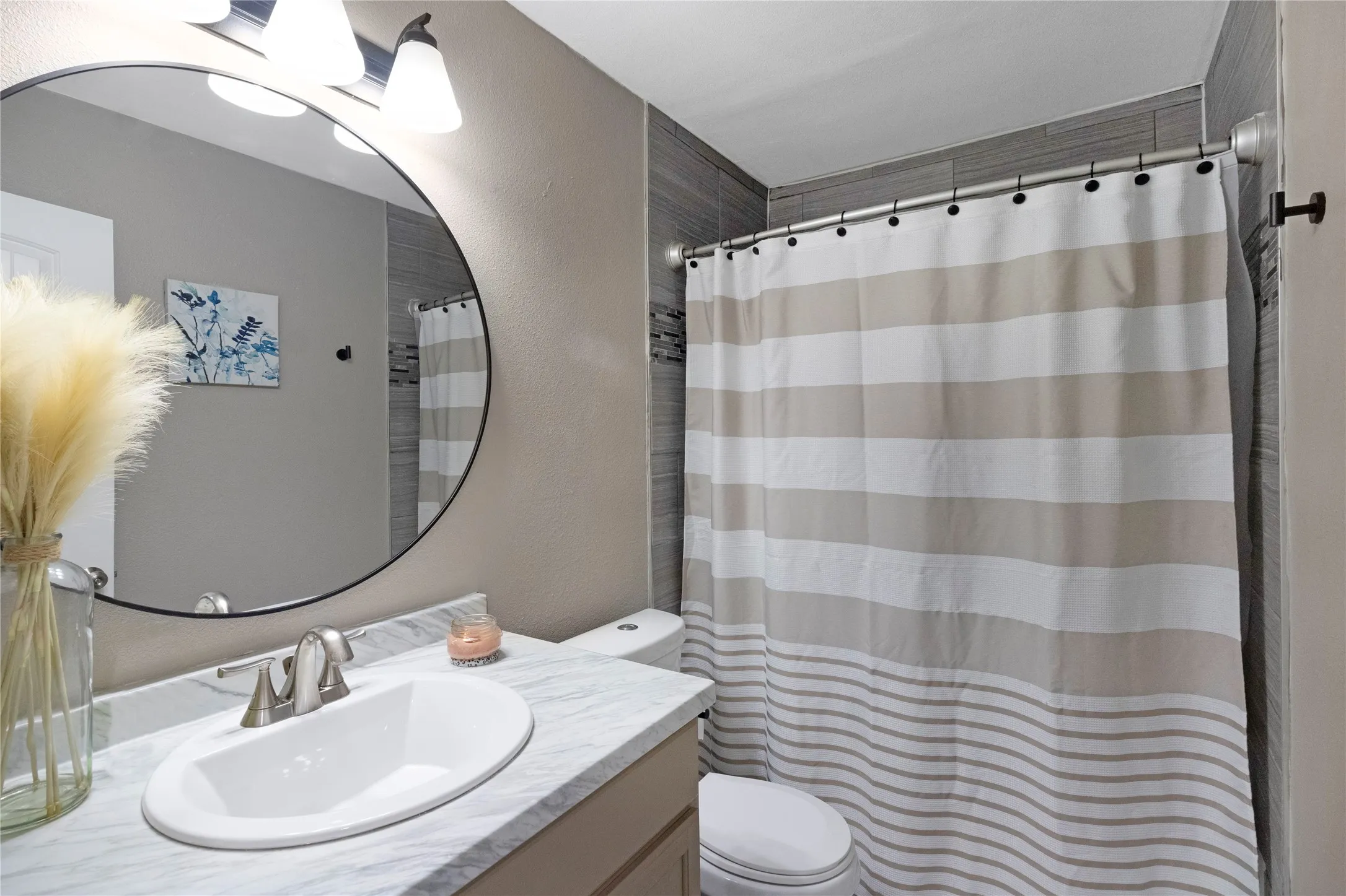 Vanity with a single oval sink, brushed nickel faucet, and a large round mirror