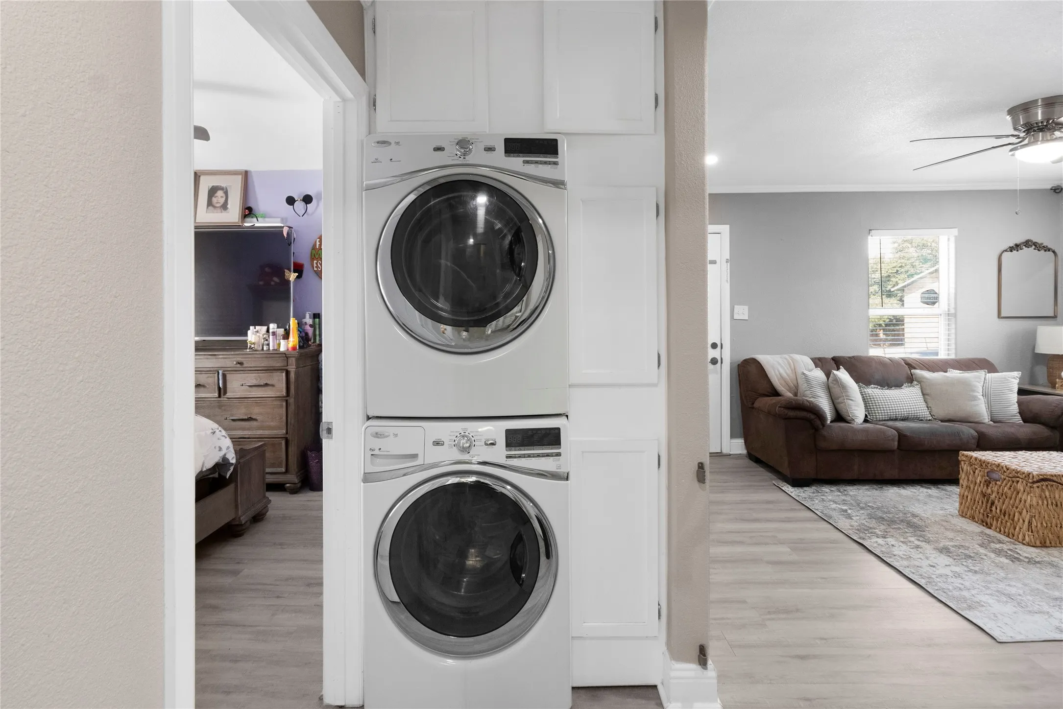 Stackable laundry appliances with built-in cabinetry, wood-finish flooring, and a ceiling fan with integrated lighting