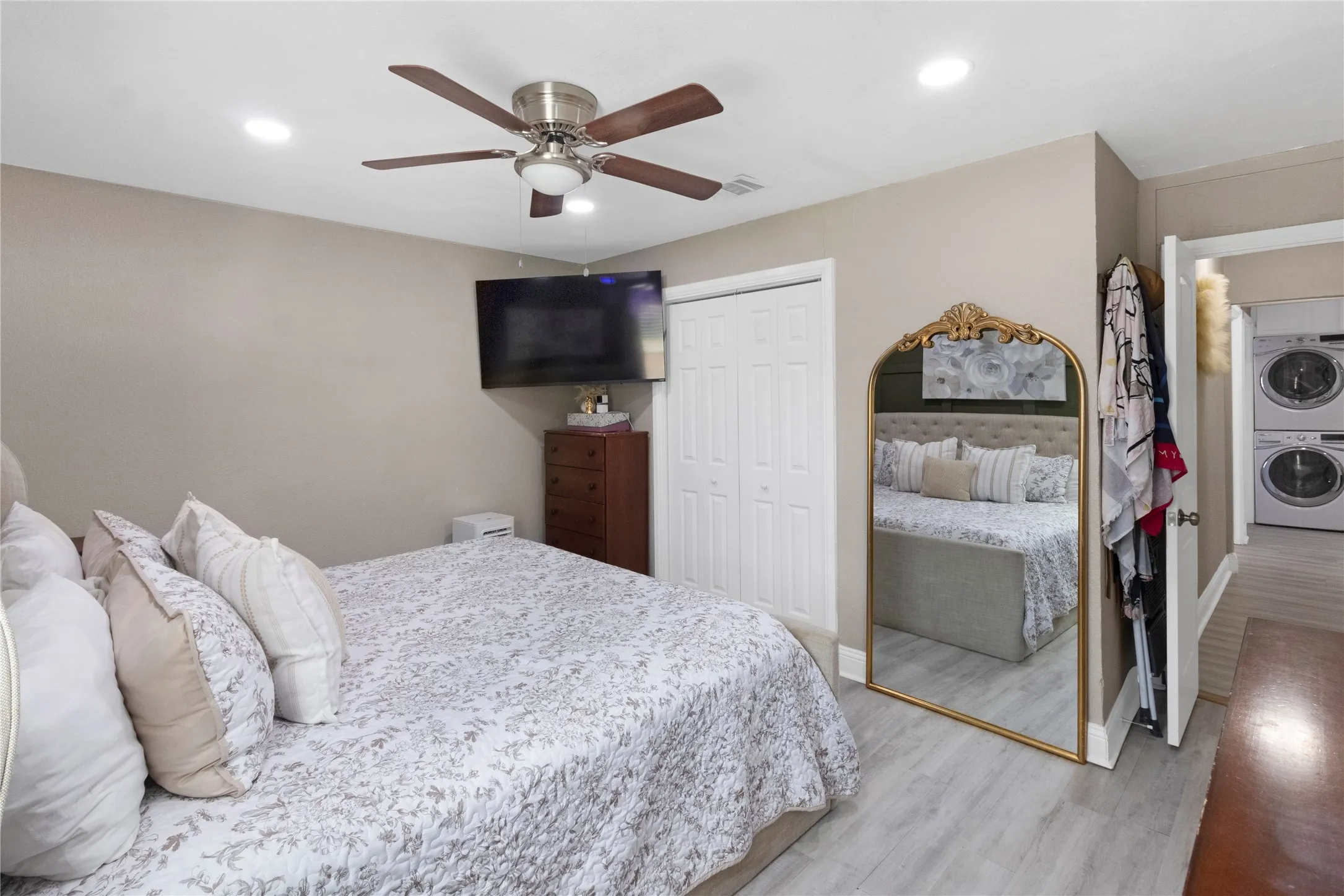 Wood-finish flooring, recessed lighting, ceiling fan, bi-fold closet doors, and an entryway with stacked appliances