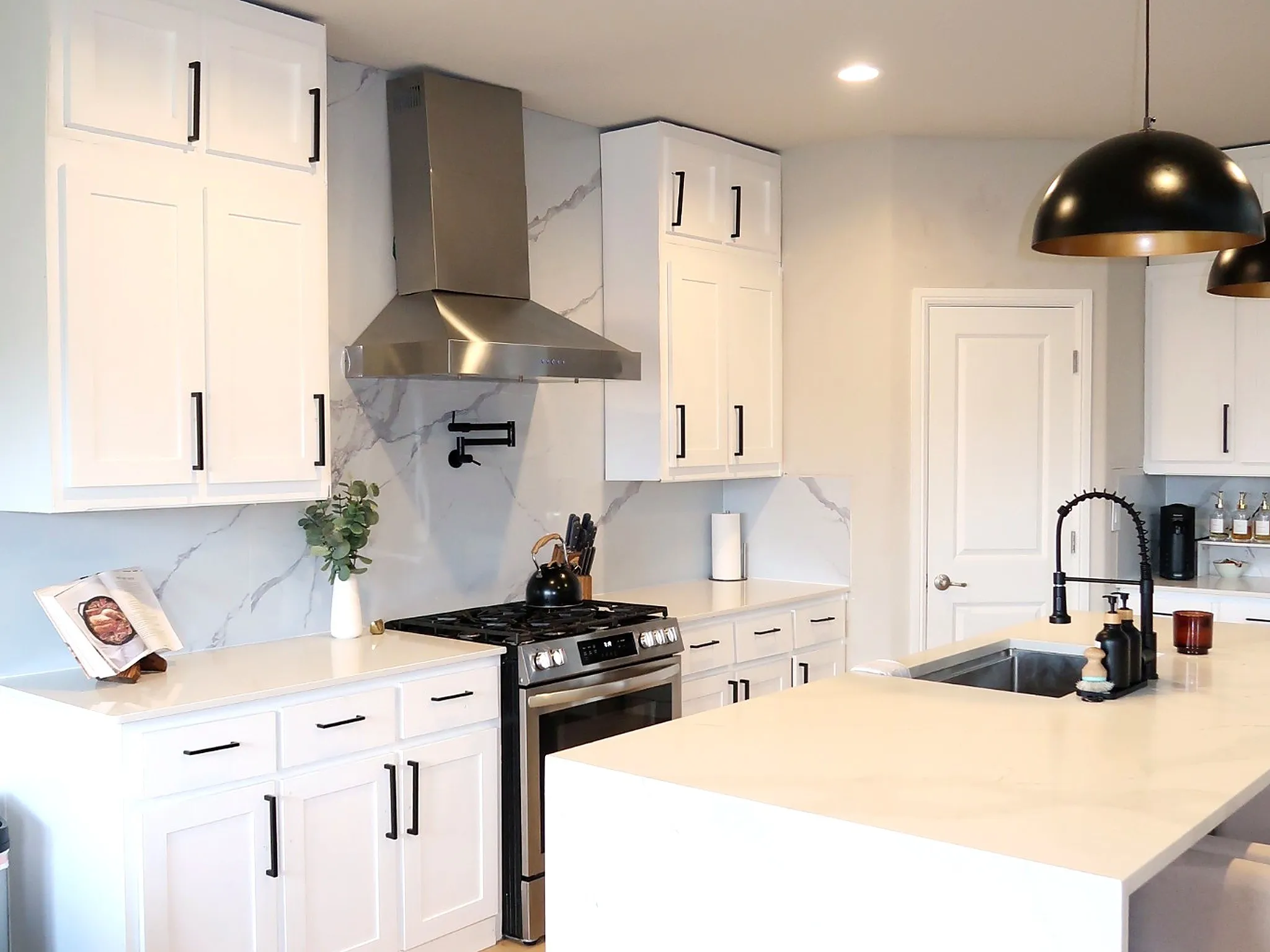 White shaker-style cabinetry with matte black hardware, stainless steel range with coordinating hood, and a pot filler