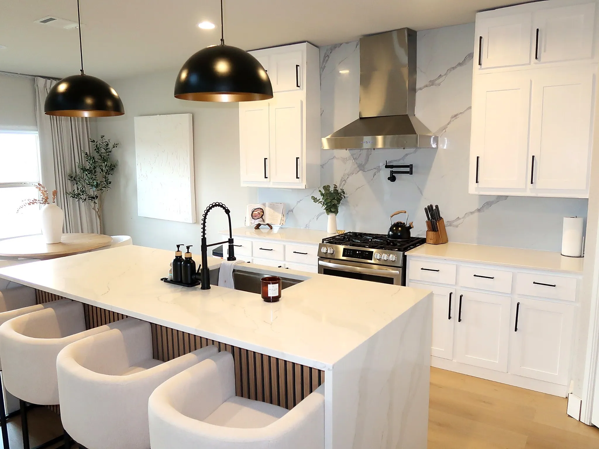 Kitchen featuring white shaker-style cabinetry with matte black hardware, a large kitchen island with a waterfall countertop, and a stainless steel appliance suite including a gas range and range hood