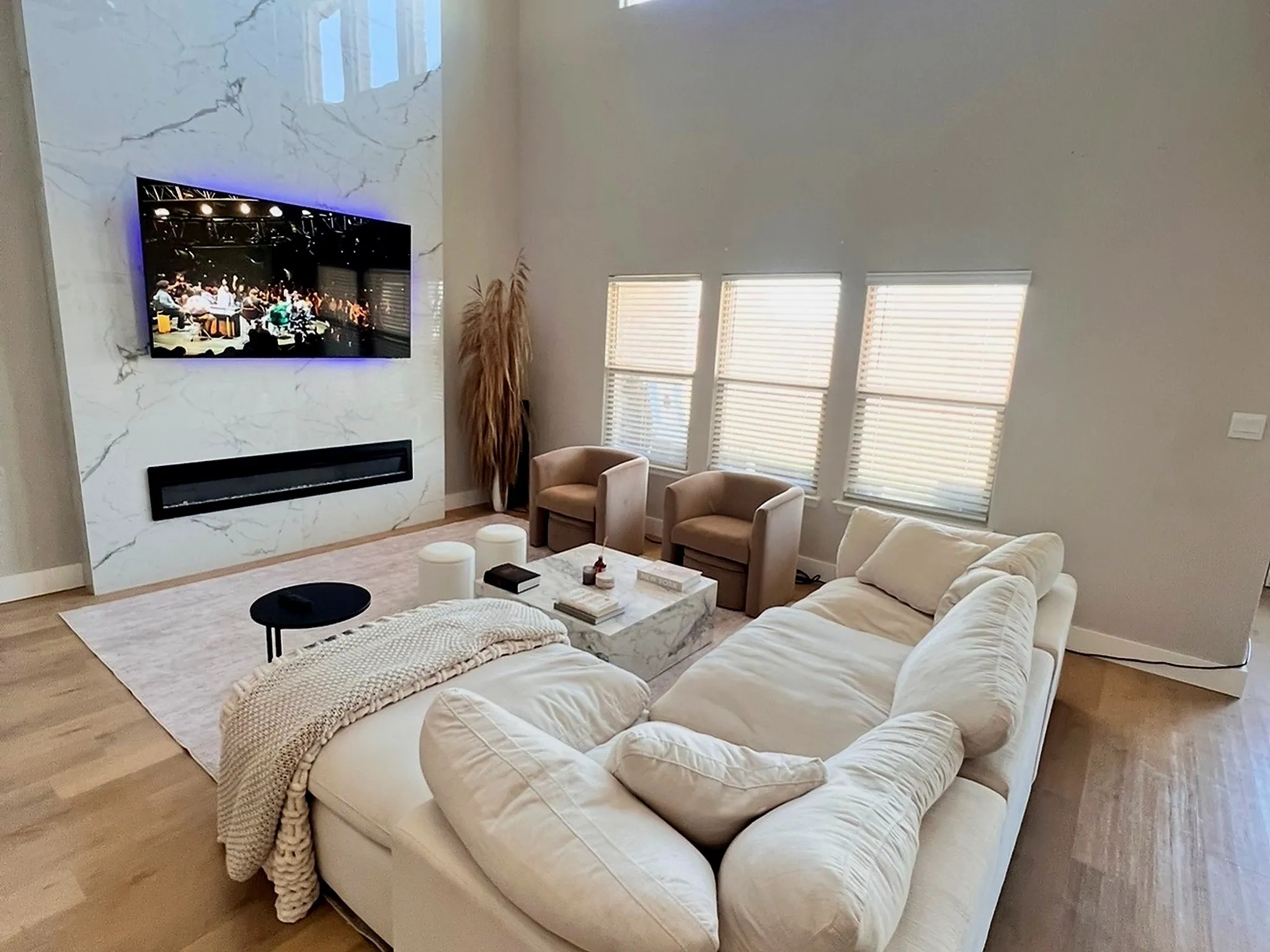High ceilings, light wood-finish flooring, and a linear electric fireplace set within a floor-to-ceiling marbled accent wall
