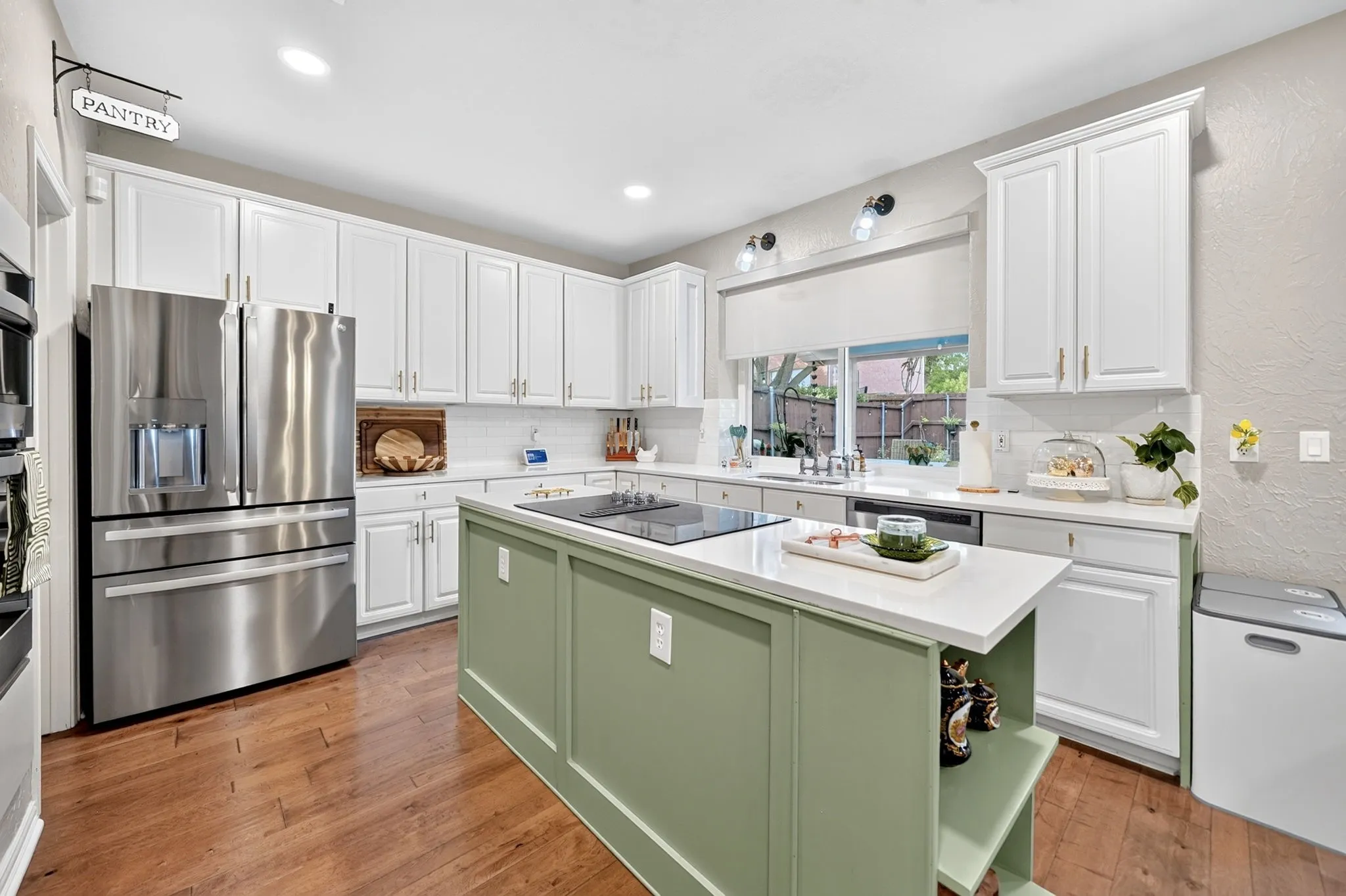White shaker cabinetry, wood-finish flooring, undermount sink, recessed lighting, and a kitchen island with built-in cooktop