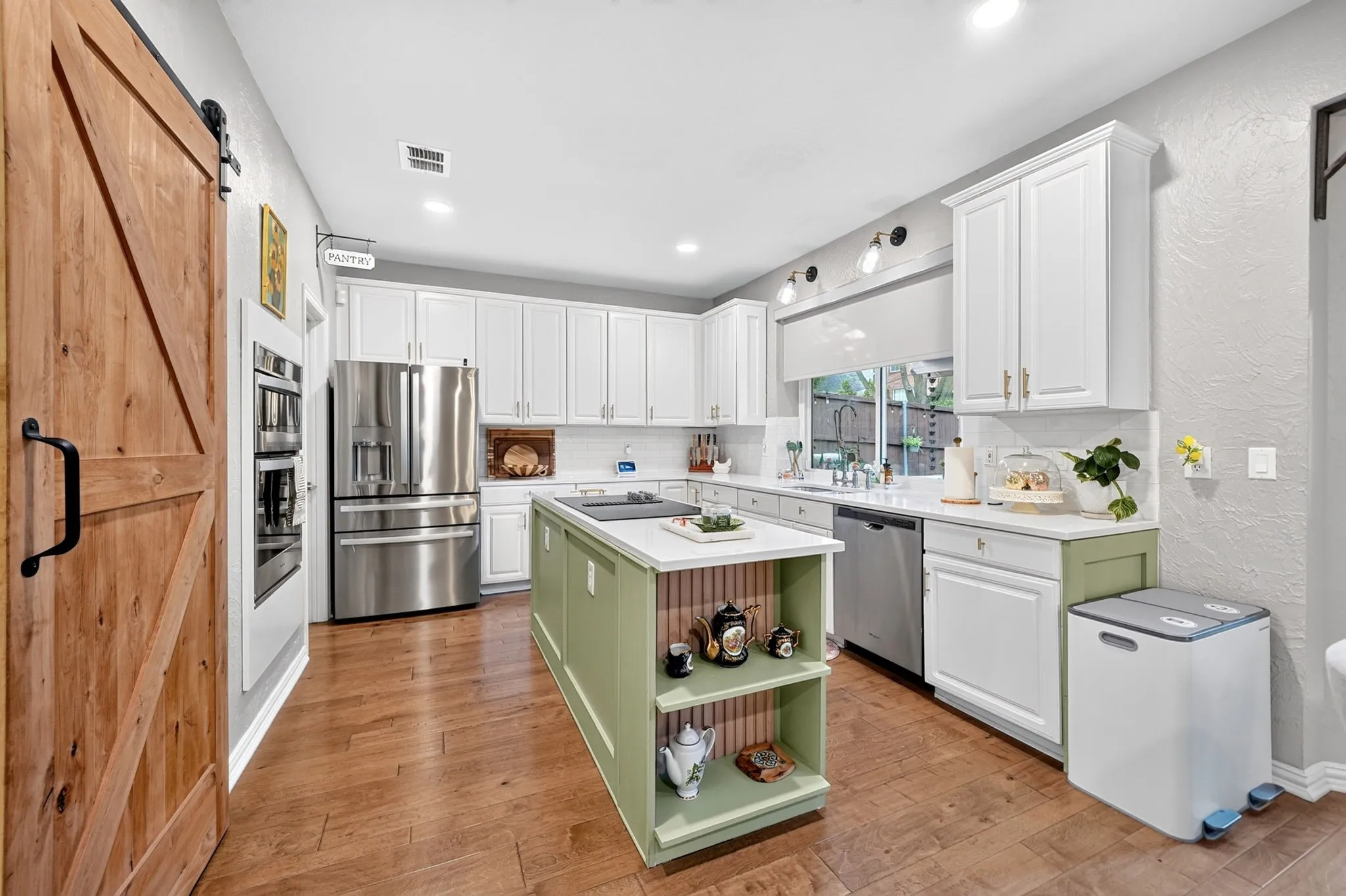Kitchen featuring wood-finish flooring, white cabinetry with gold-tone hardware, stainless steel appliances, and a central island with open shelving