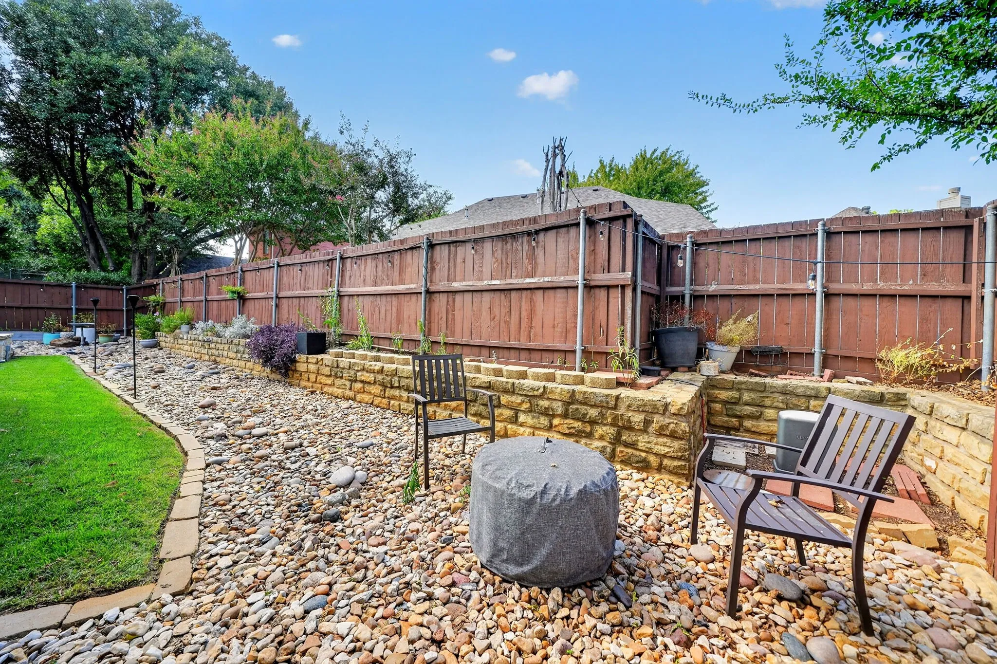 Expansive backyard featuring a manicured lawn, stone-lined pathways, and a tiered stone retaining wall
