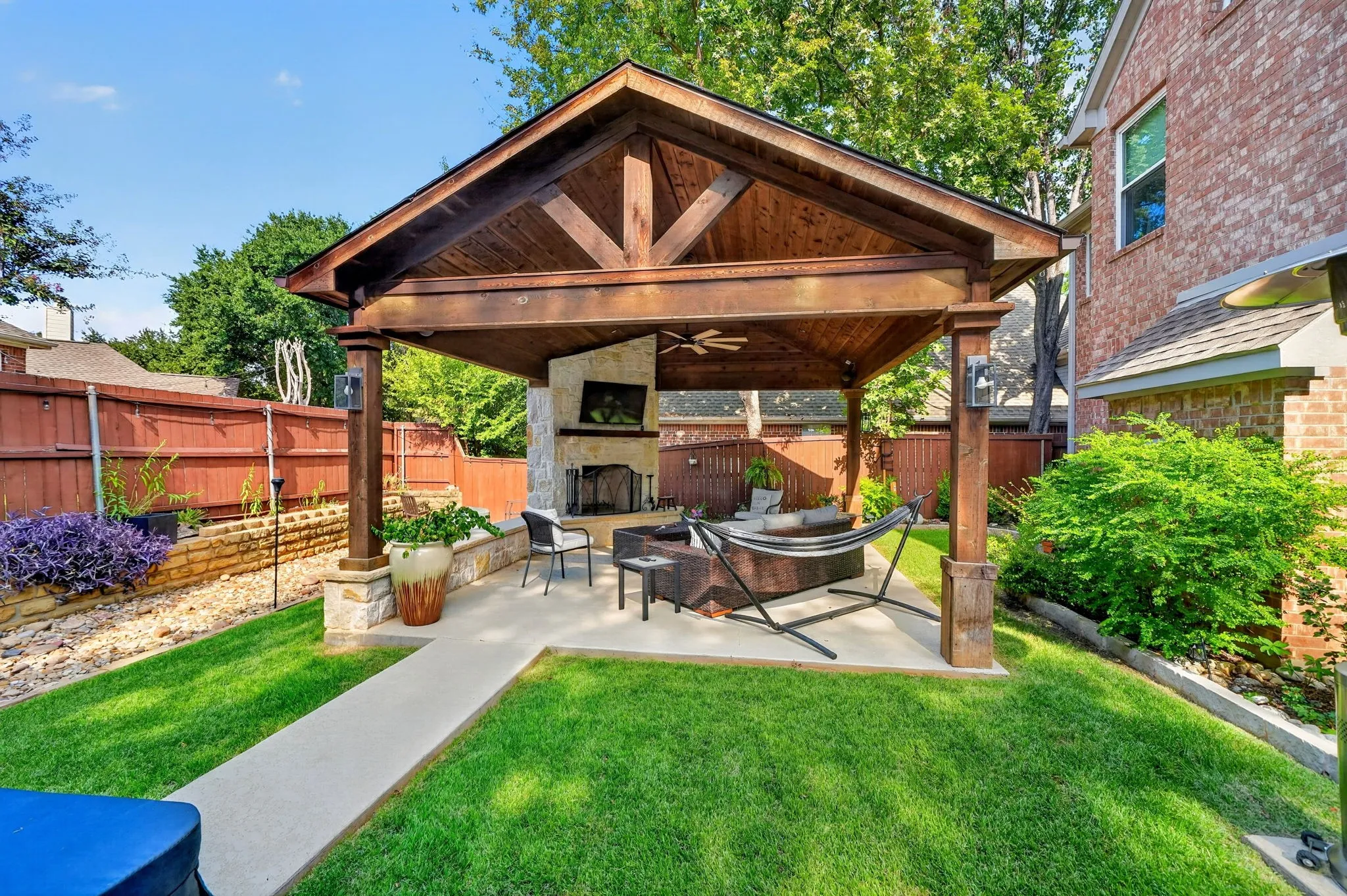 Covered patio with a wood-beam ceiling, built-in fireplace, and stone-clad columns