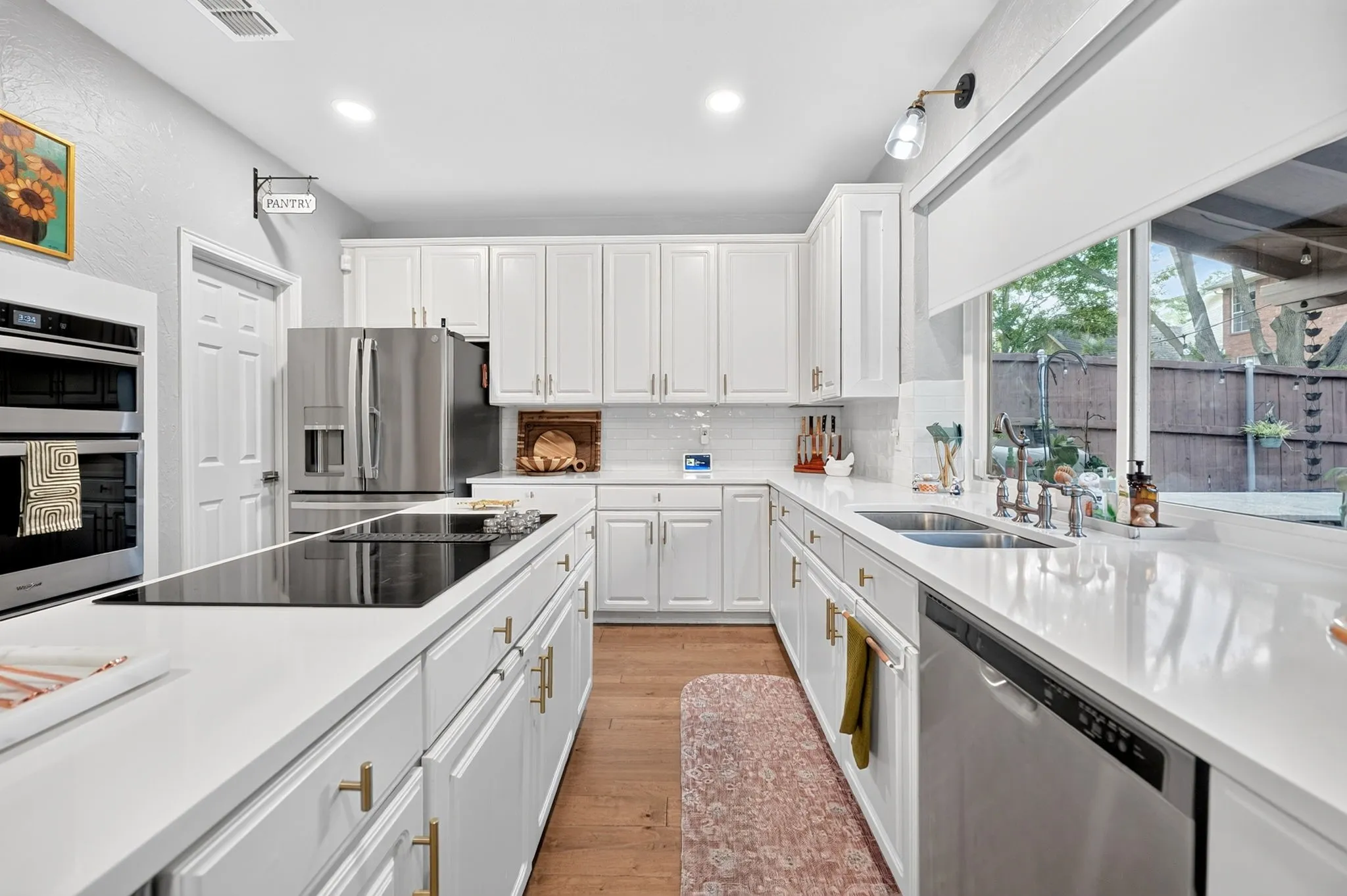 White cabinetry with gold-finish hardware, stainless steel appliances, wood-finish flooring, and white countertops