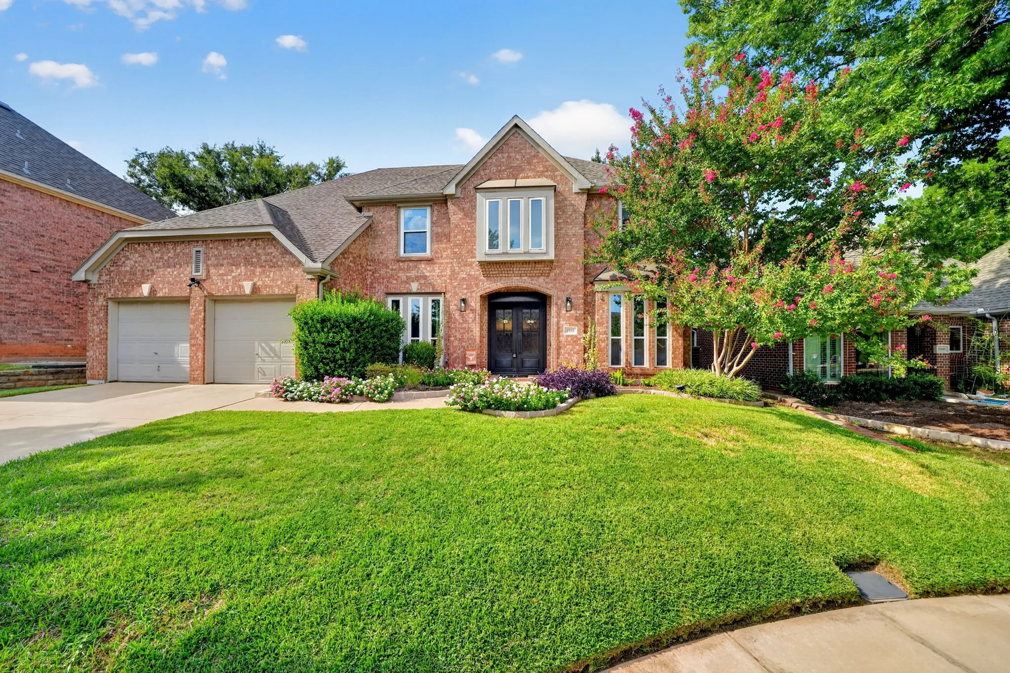 Brick exterior with a gabled roofline, two-car garage, manicured lawn, established landscaping, and a bay window