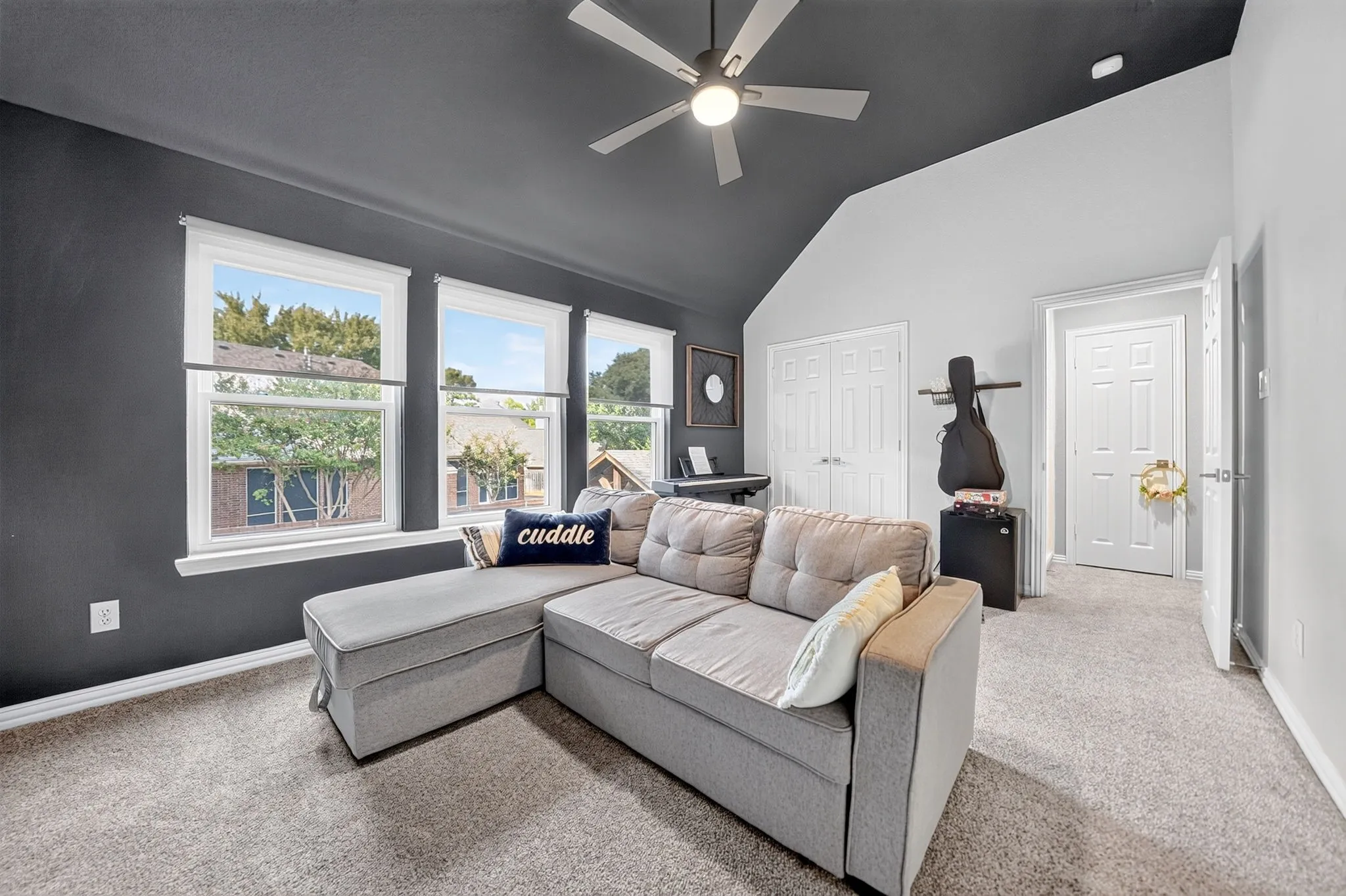 Vaulted ceiling with a ceiling fan, multiple windows with white trim, gray carpet flooring, and two panel doors