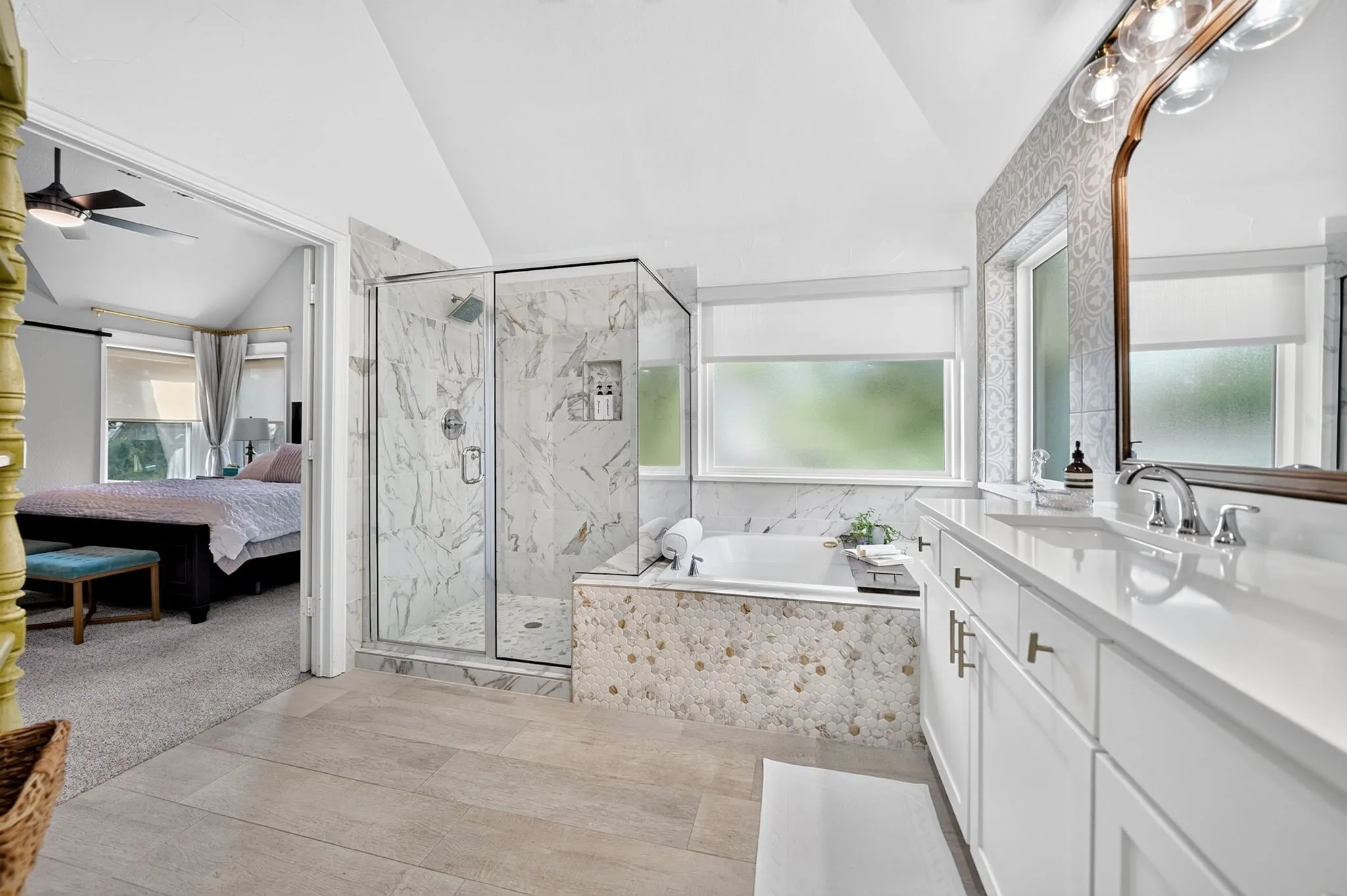 Tiled walk-in shower with a glass enclosure, soaking tub with decorative tile surround, dual vanity with undermount sinks, and light wood-finish flooring