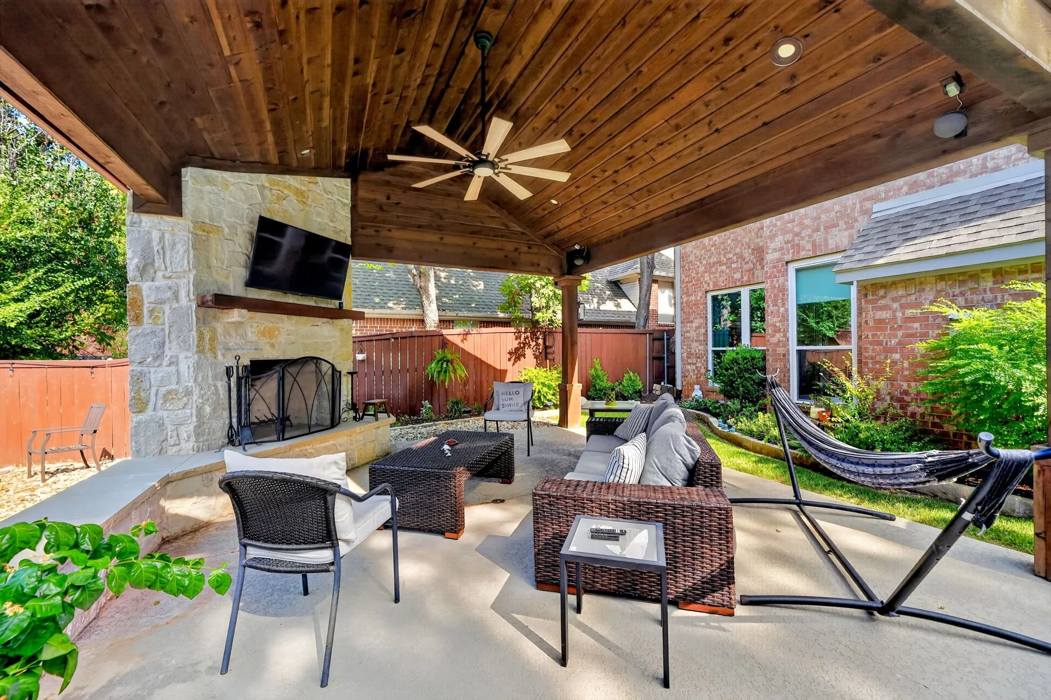 Expansive covered patio featuring a stone fireplace, wood-plank ceiling, ceiling fan, and recessed lighting