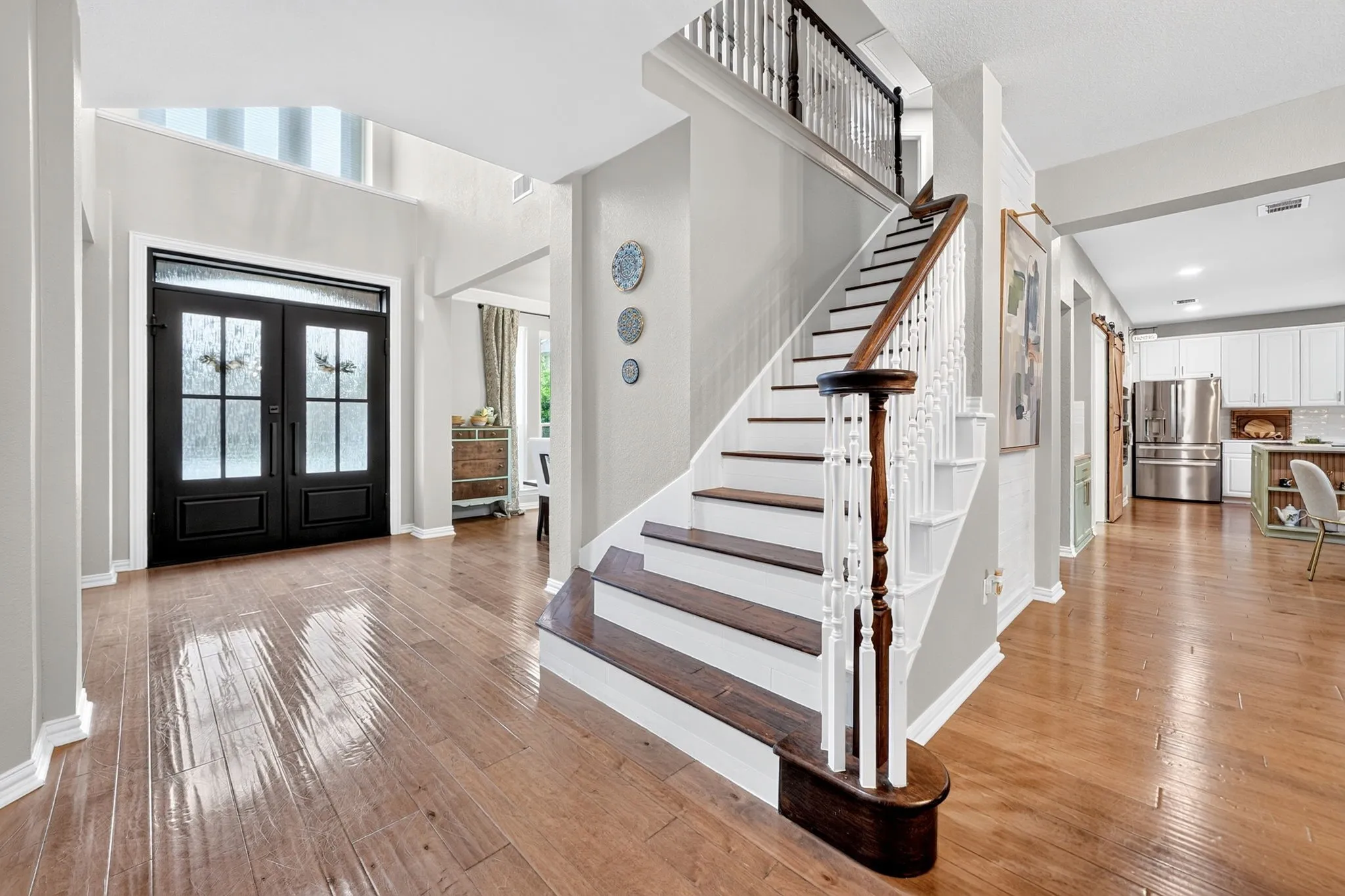 Wood-finish flooring, dual entry doors with frosted glass, and a grand staircase with dark wood treads and white risers