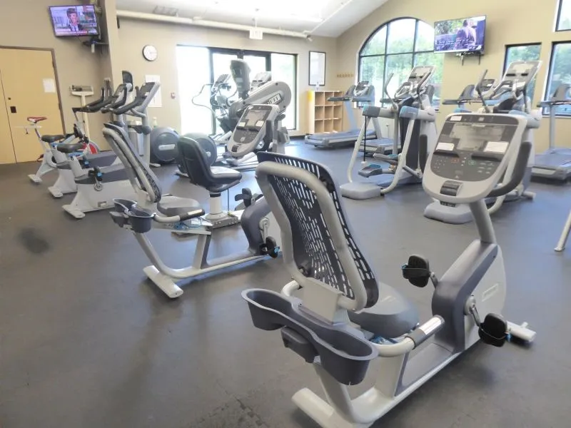 Community Fitness center featuring exercise equipment, vaulted ceiling, arched window, and durable flooring
