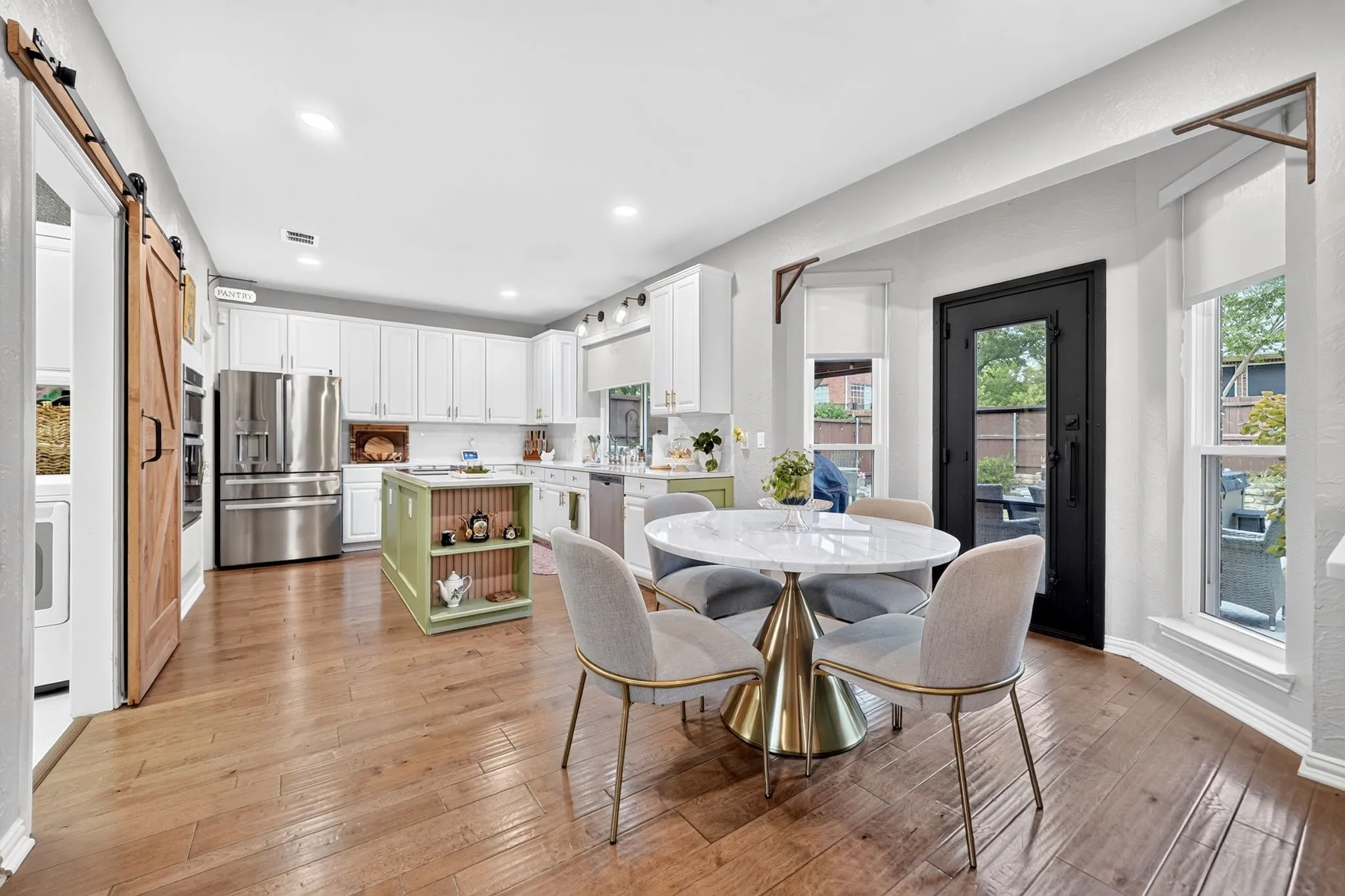 Wood-finish flooring throughout, bright white kitchen cabinetry, stainless steel appliances, custom green kitchen island, and a black-framed glass-panel door