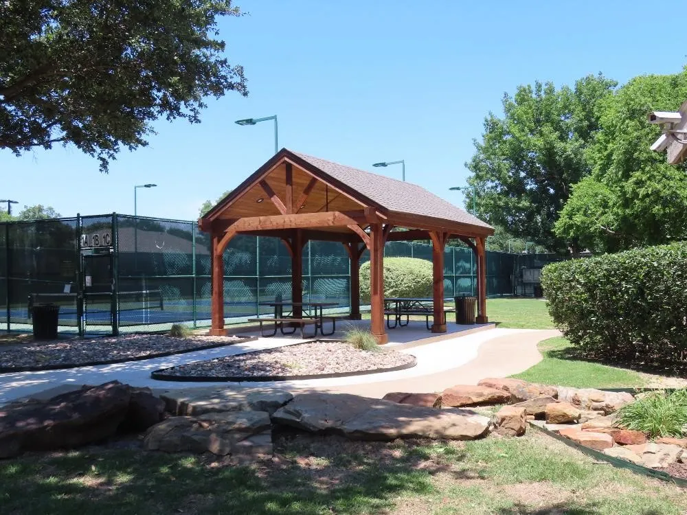 Community Wood-frame gazebo with covered seating, concrete pathway, and tennis courts with lighting