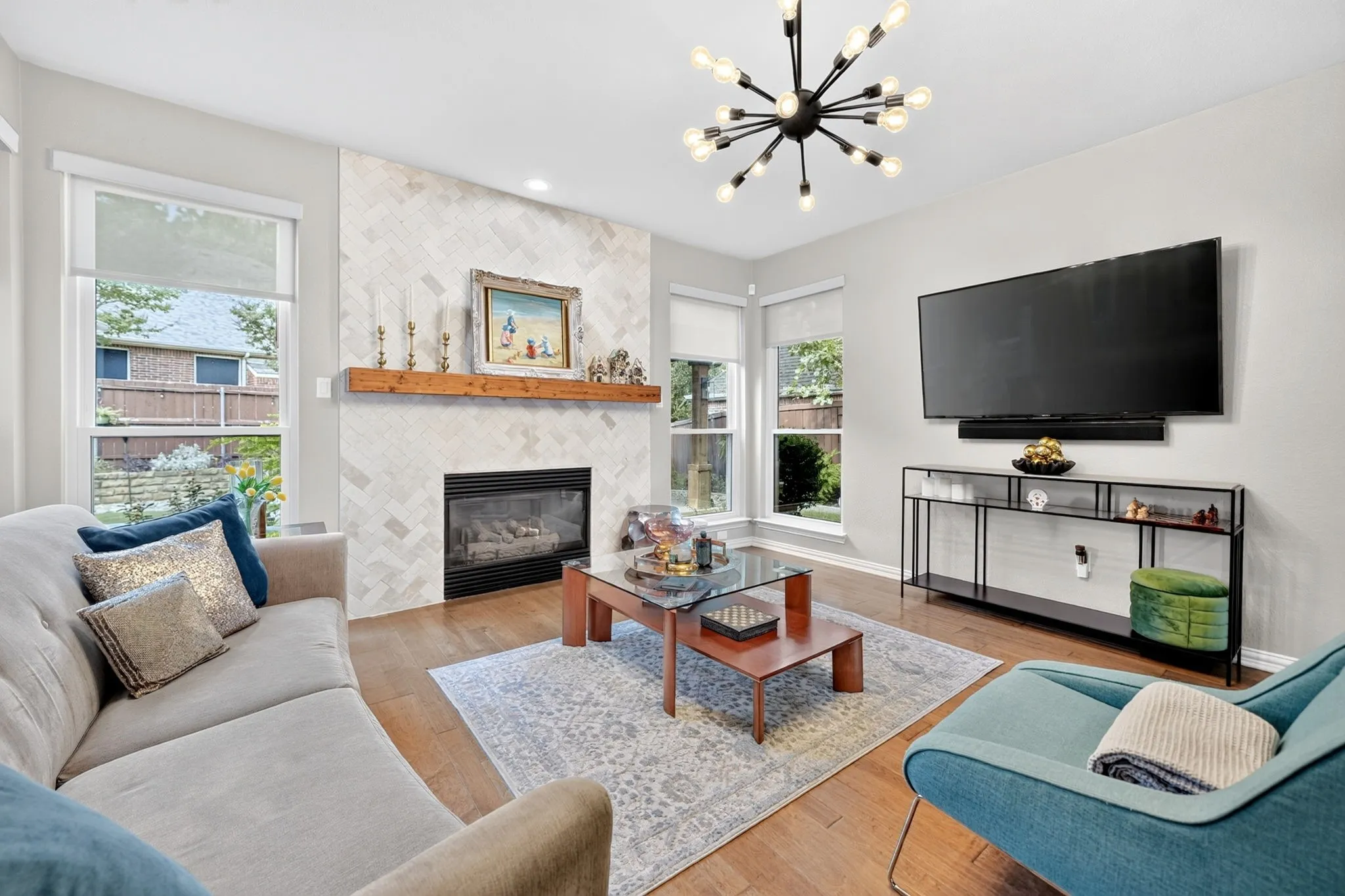 Herringbone tile fireplace with a wood mantle, wood-finish flooring, and a contemporary chandelier