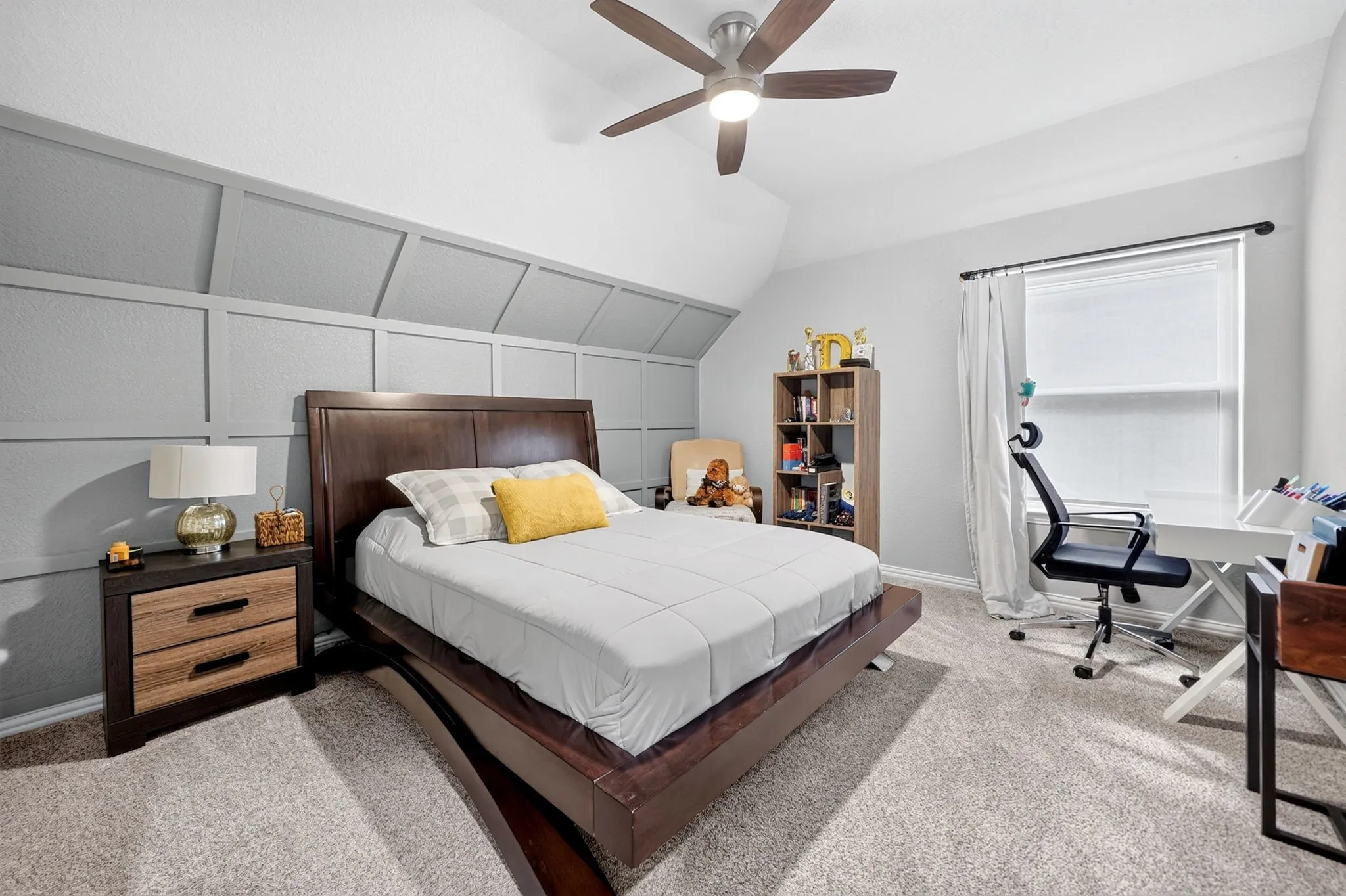 Ceiling fan with integrated lighting, textured wall paneling, window with roller shade, and neutral-toned carpeting