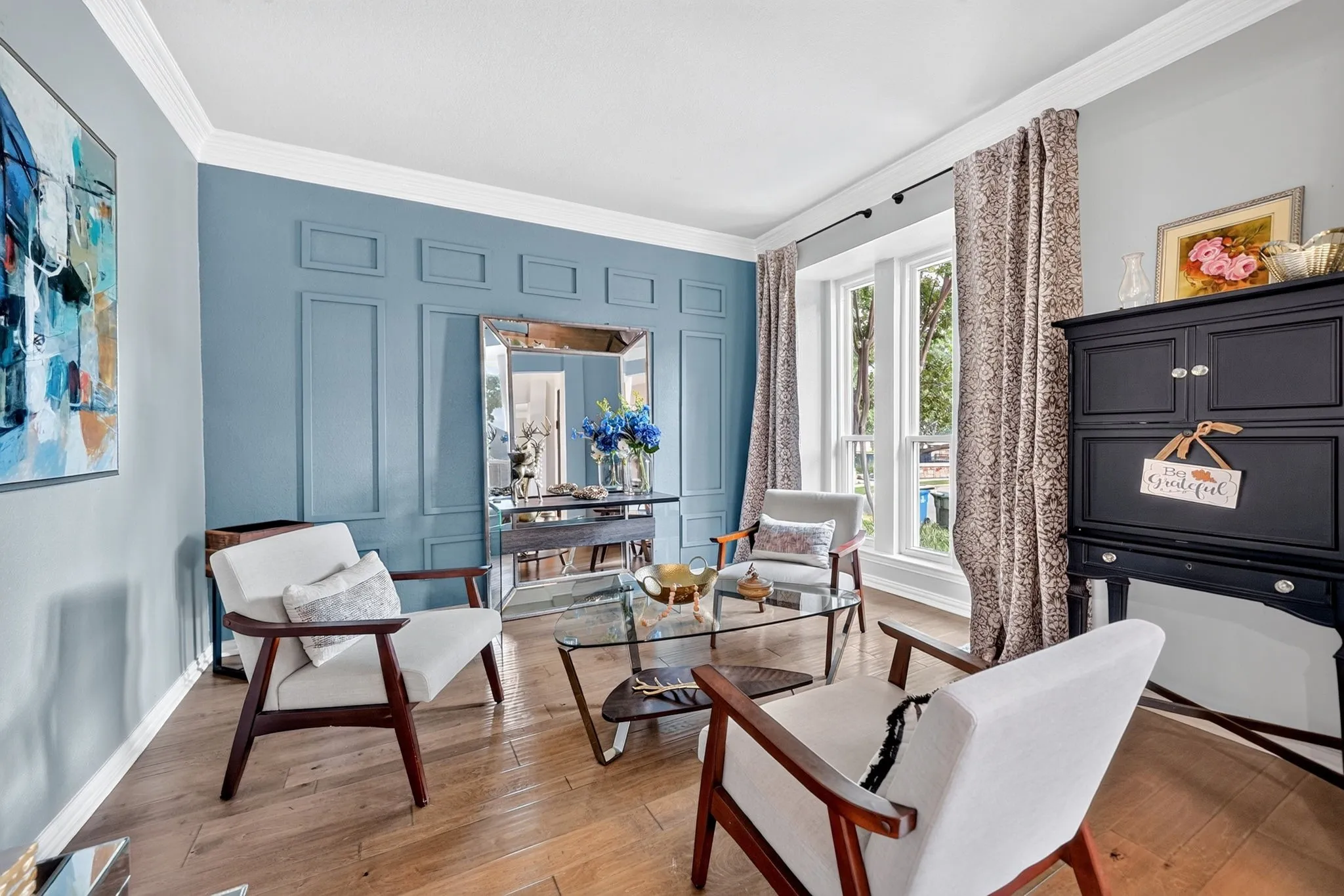 Wood-finish flooring, accent wall with panel molding, crown molding, and bay window