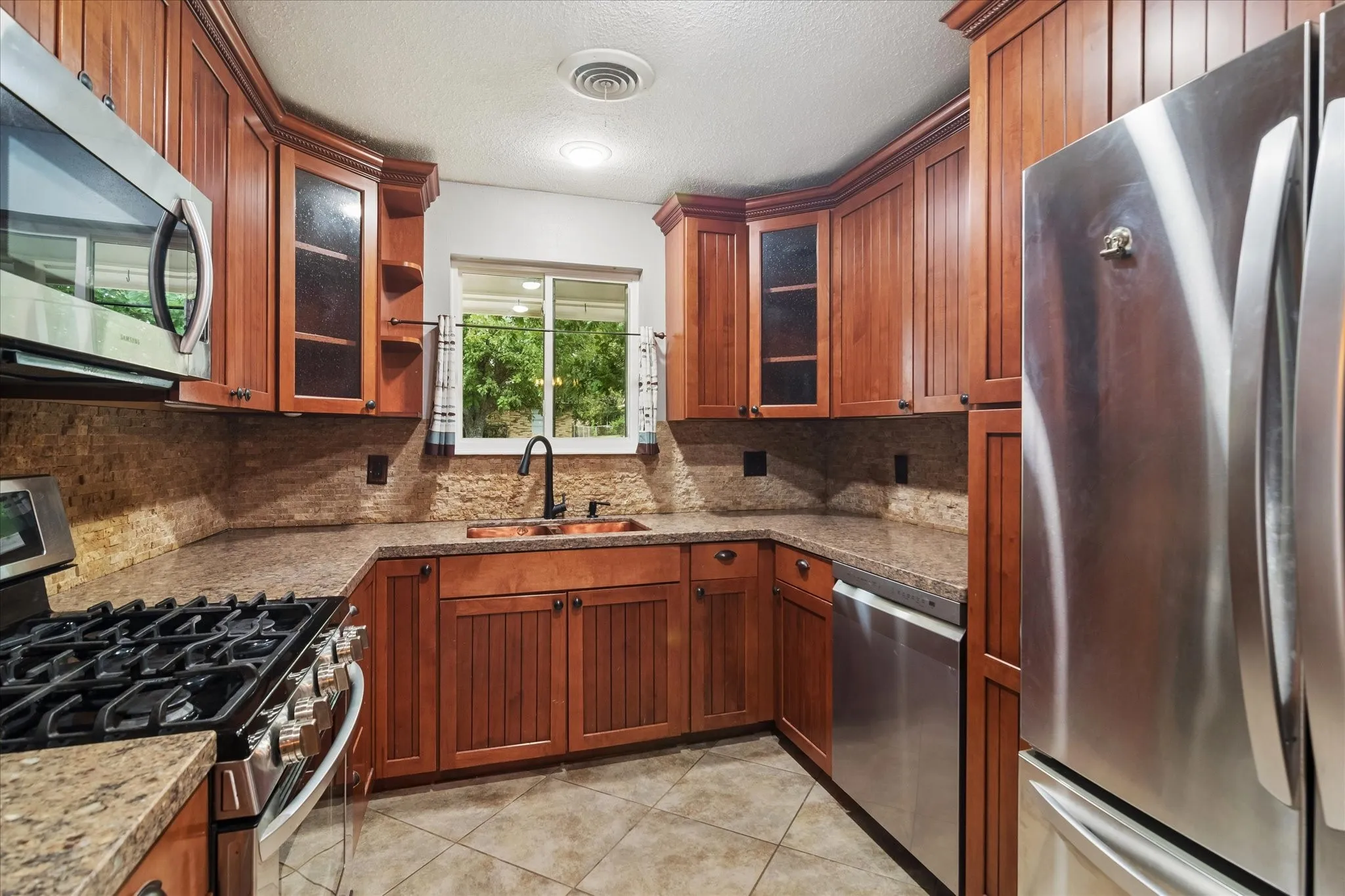 Updated kitchen with granite countertops, stacked-stone backsplash, a copper sink, and stainless-steel appliances including a gas range and a breakfast area.