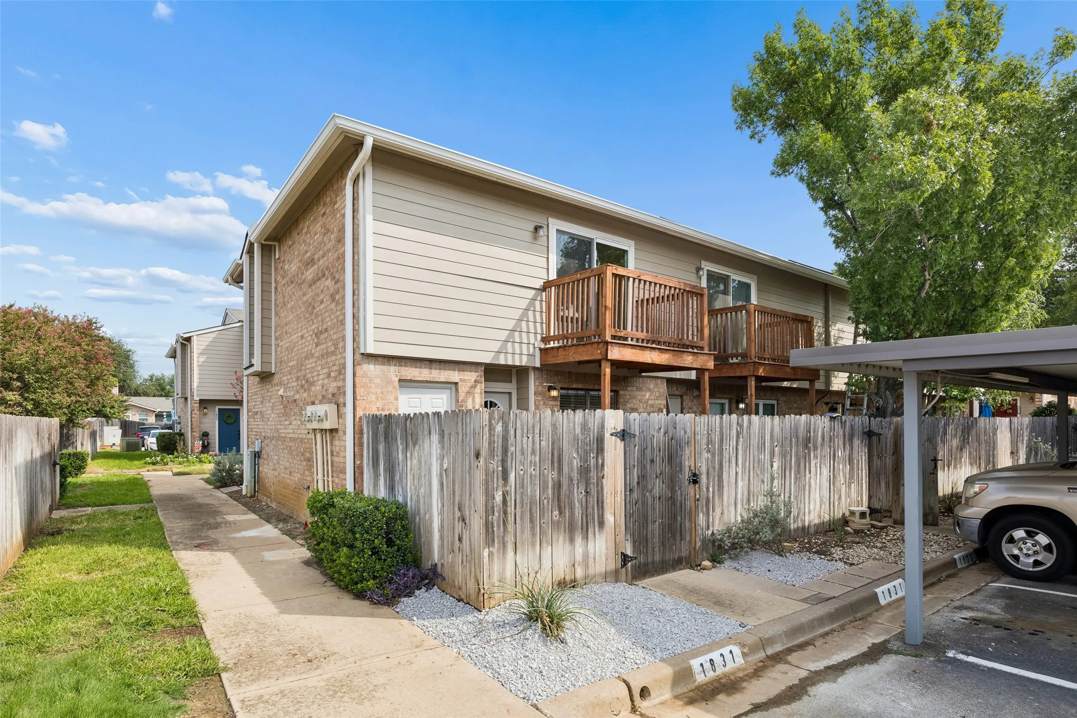 Brick and siding exterior featuring individual wood-fenced patios, private wooden balconies, and covered parking
