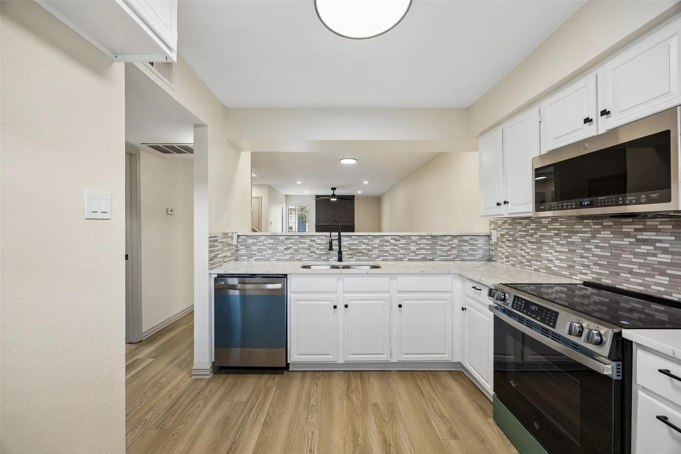 Kitchen featuring white cabinetry, stainless steel appliances, a mosaic tile backsplash, light-toned countertops, and wood-finish flooring
