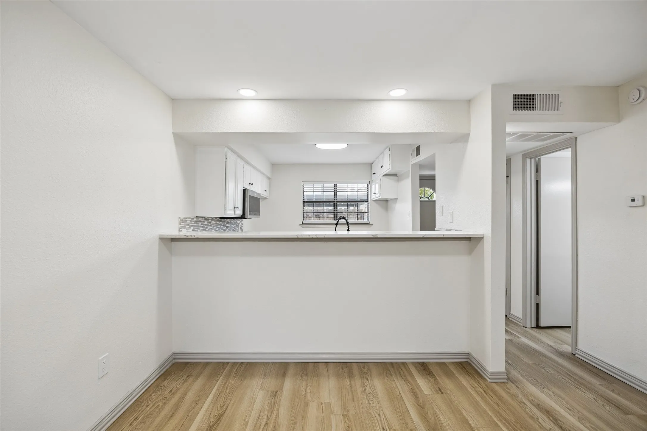Wood-finish flooring, recessed lighting, and a kitchen pass-through with a breakfast bar