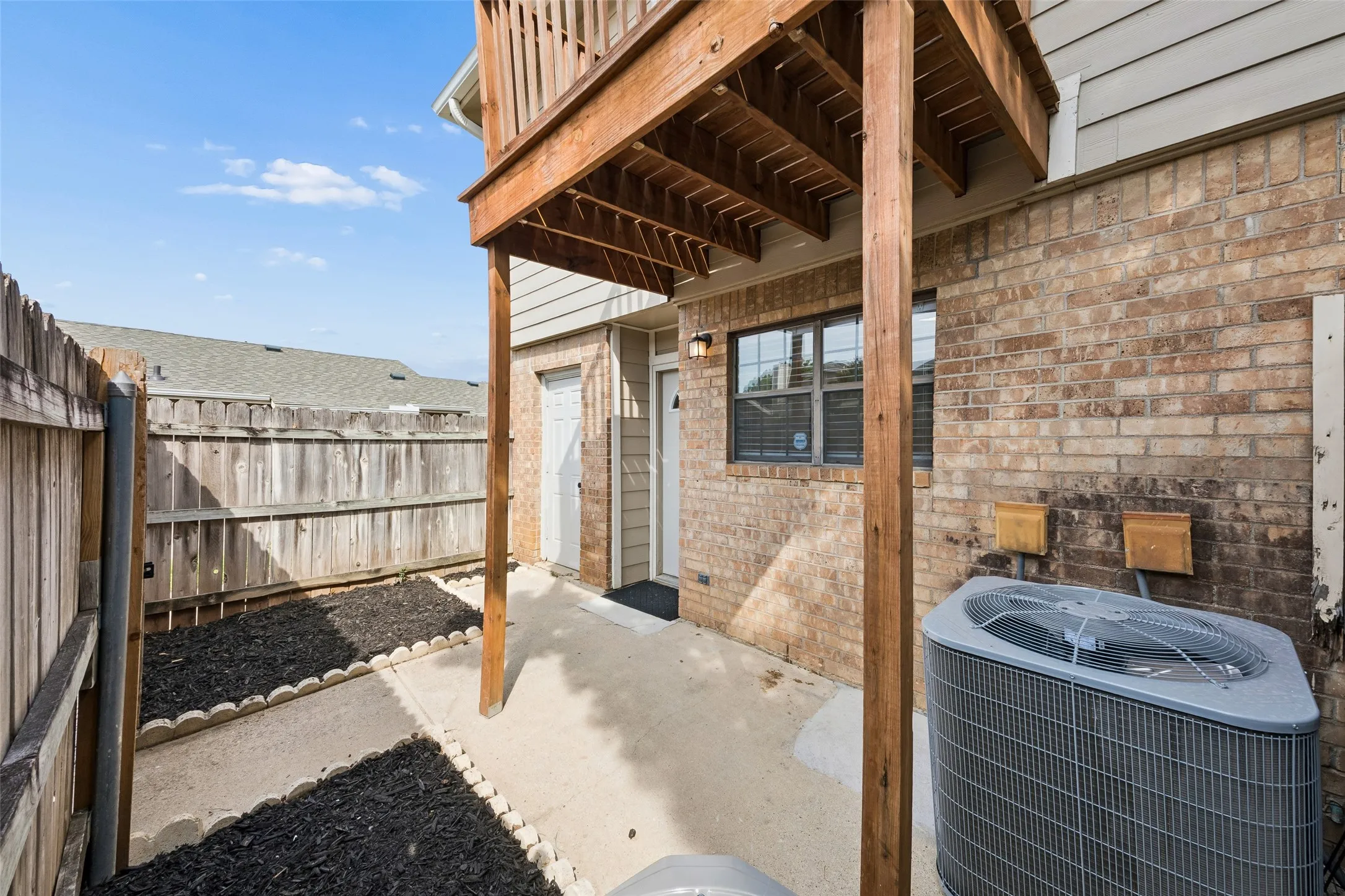 Paved patio area, brick exterior, upper-level wood deck, wood privacy fencing, and an exterior entry door