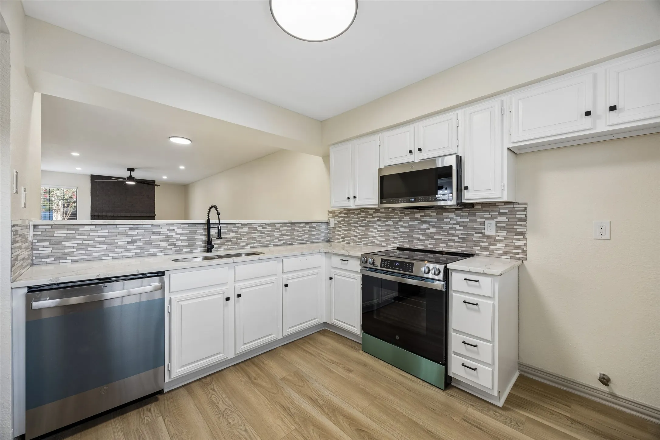 Kitchen featuring light wood-finish flooring, white cabinetry, integrated stainless steel appliances, a tiled backsplash, and light-toned countertops