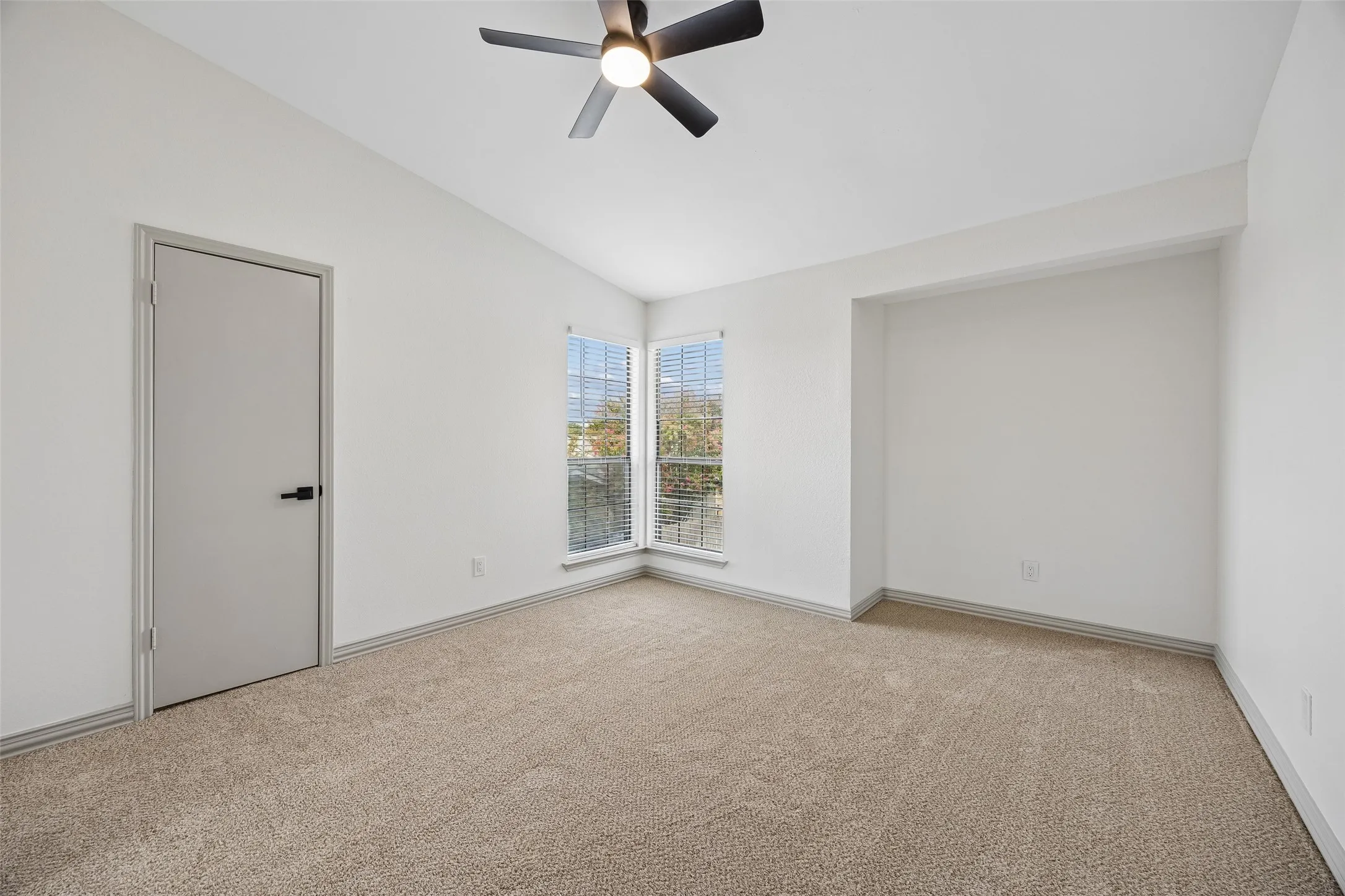 White walls with neutral carpet flooring, a modern ceiling fan, and a built-in recessed area