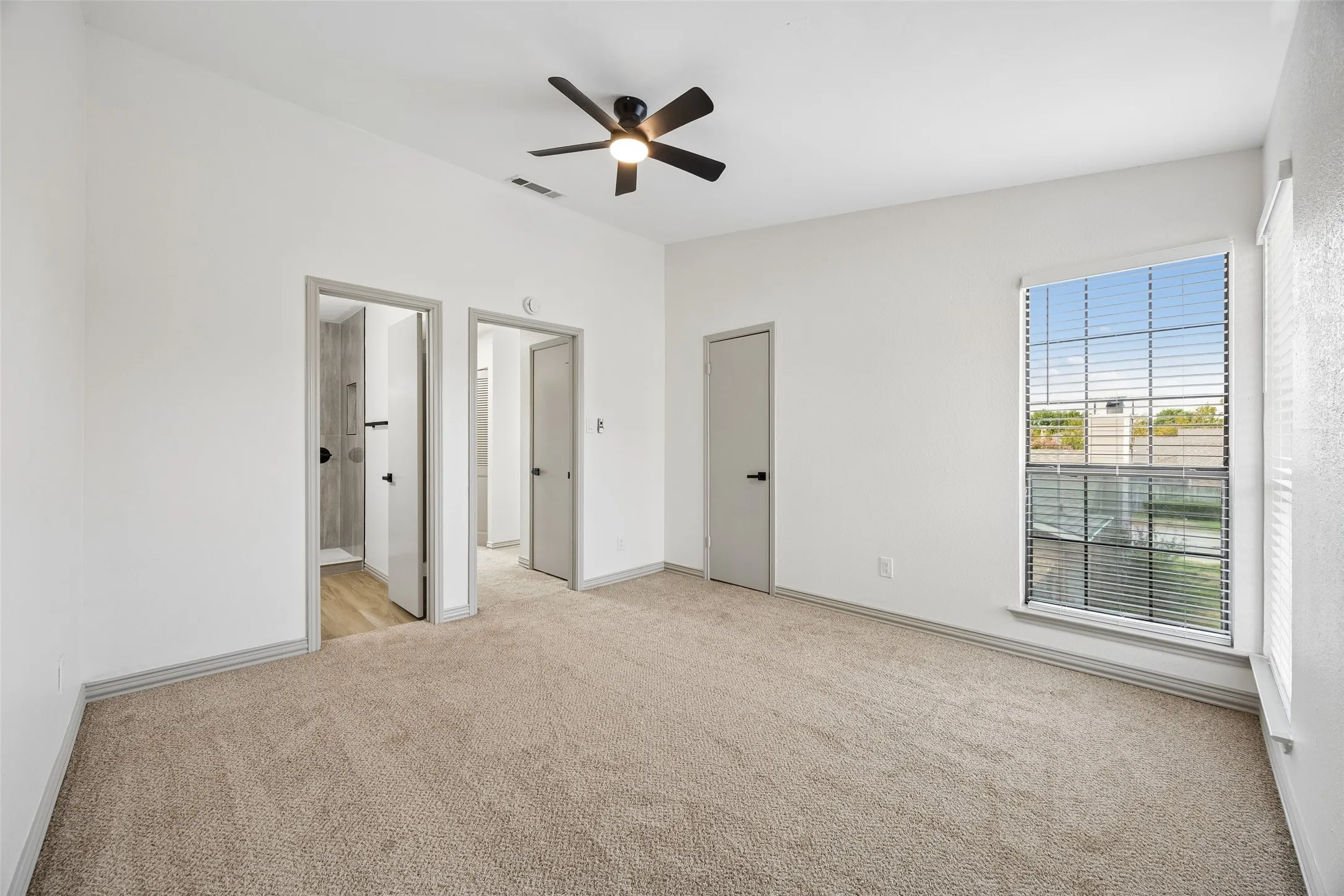 Carpeted room with a ceiling fan, multiple doorways, and a window with blinds
