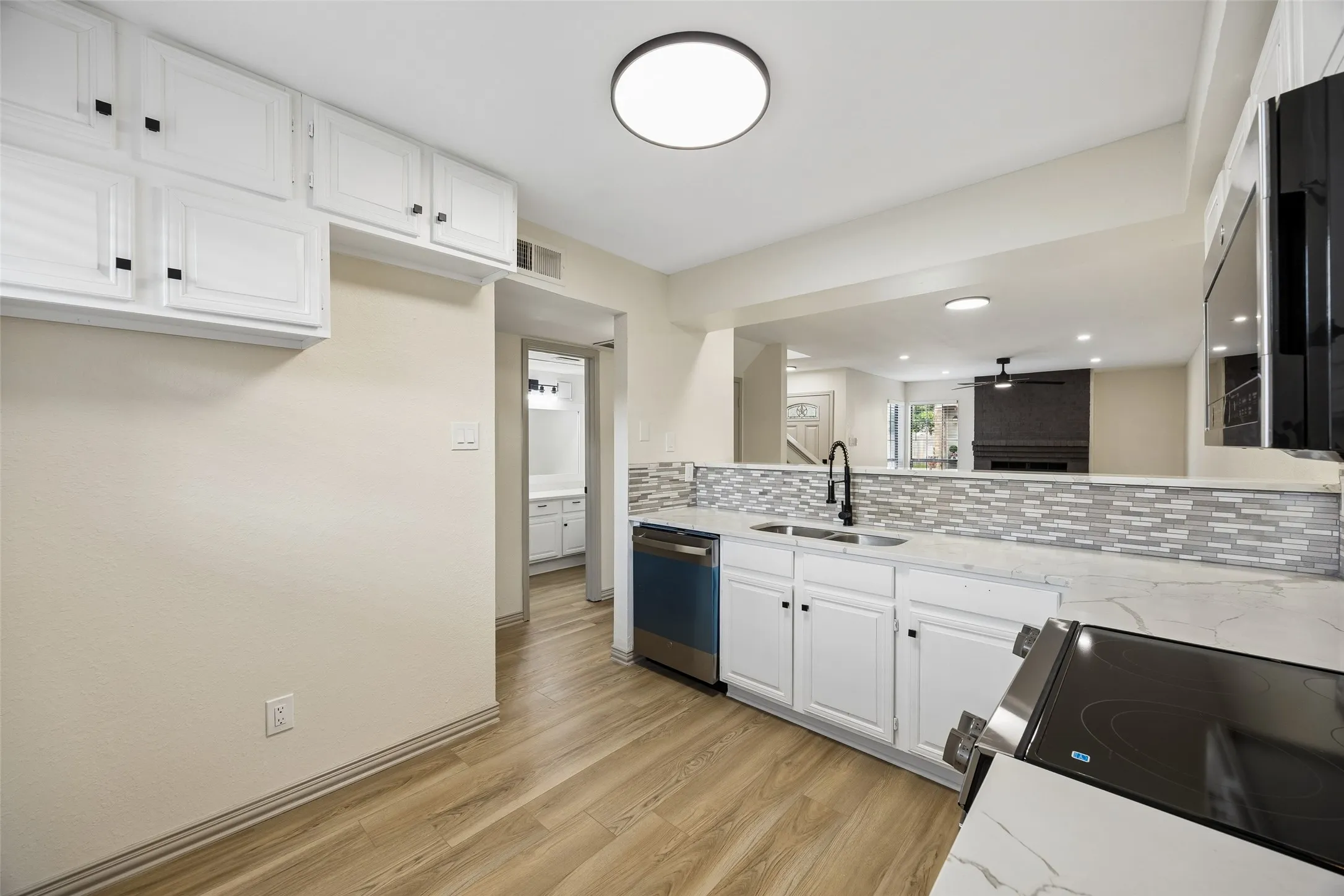 White cabinetry, wood-finish flooring, stainless steel appliances, mosaic tile backsplash, and light-toned countertops