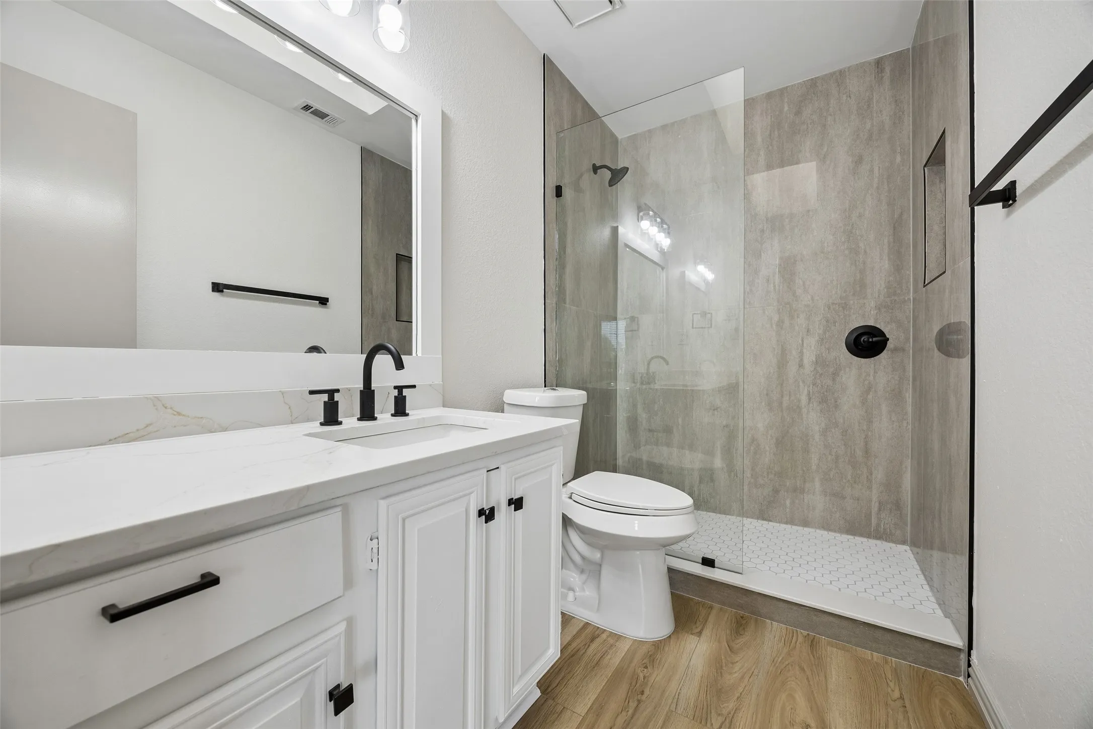 Contemporary bathroom featuring a walk-in shower with glass enclosure, single vanity with white cabinetry, and wood-finish flooring